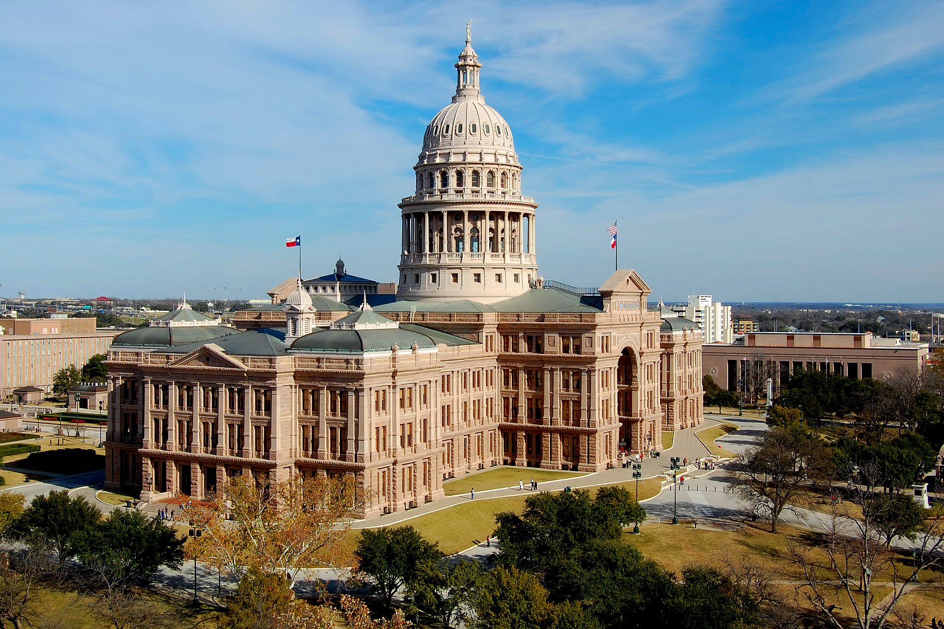 Texas State Capitol building with a large dome and columns, surrounded by trees and a blue sky