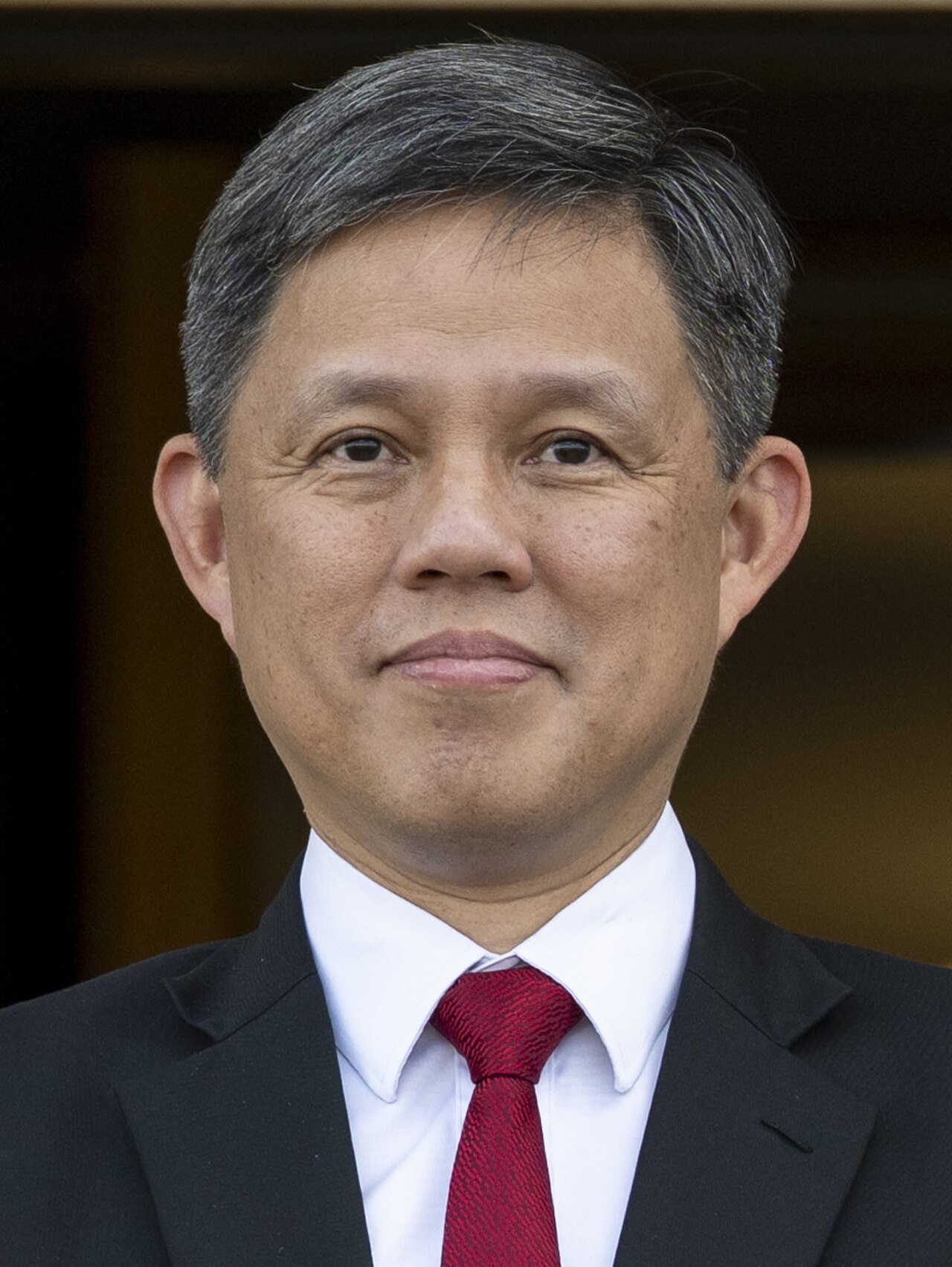 A man in a black suit, white shirt, and red tie
