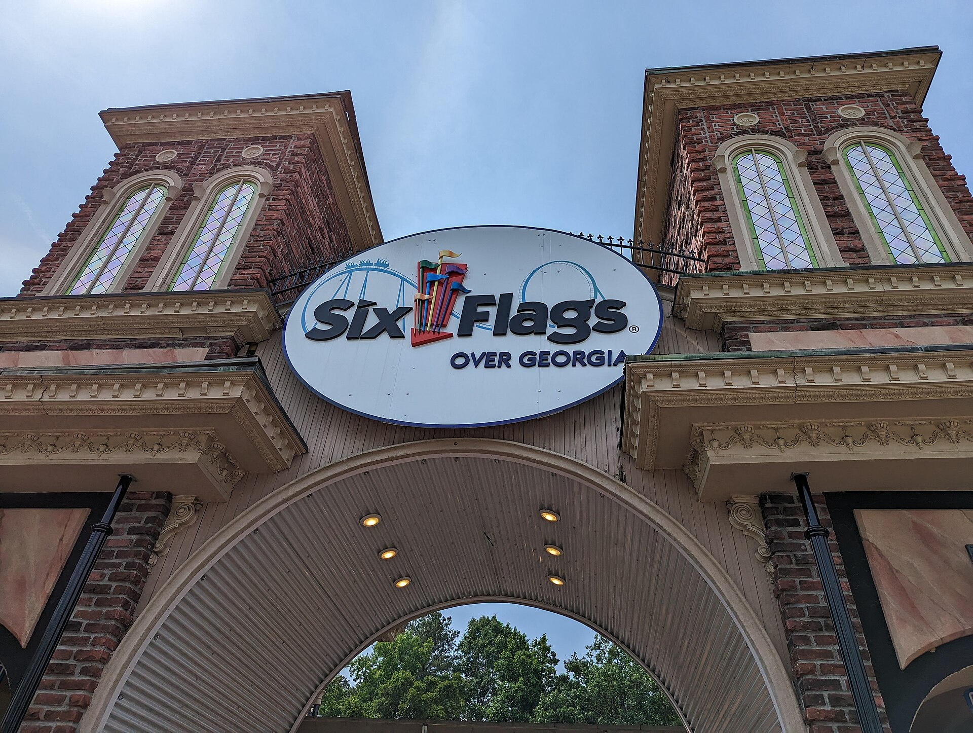 The Six Flags Over Georgia logo is displayed on a white oval sign, flanked by two brick towers with arched, stained-glass windows.