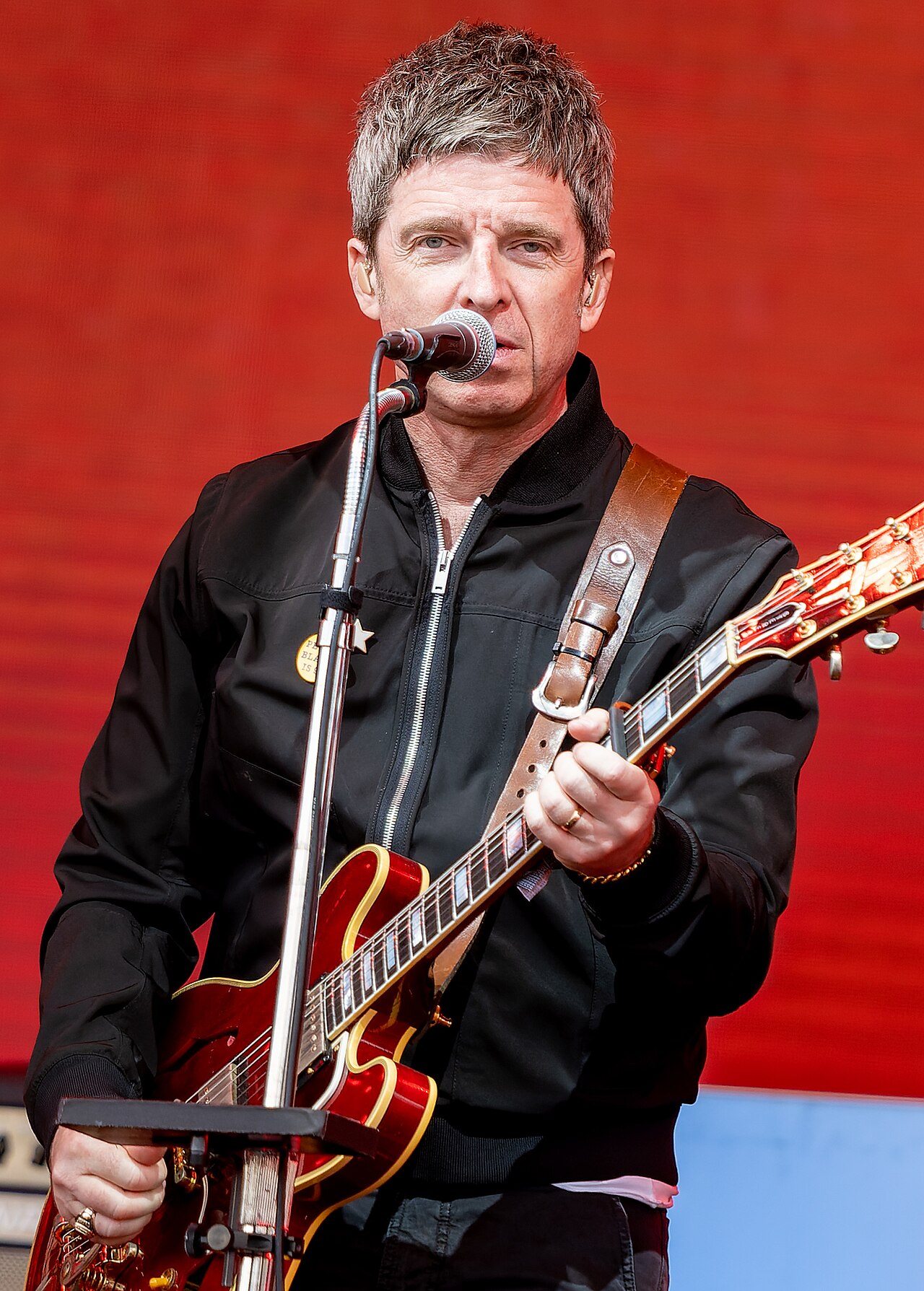 Noel Gallagher playing guitar and singing into a microphone