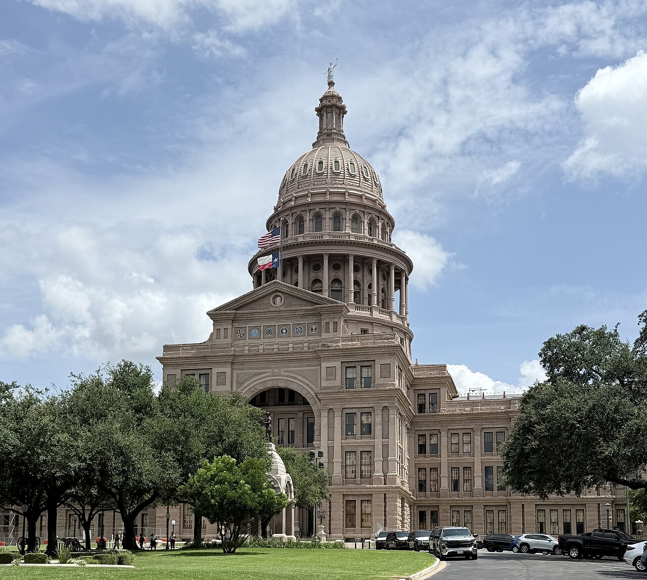 Texas State Capitol building with dome and columns, surrounded by trees and parking lot