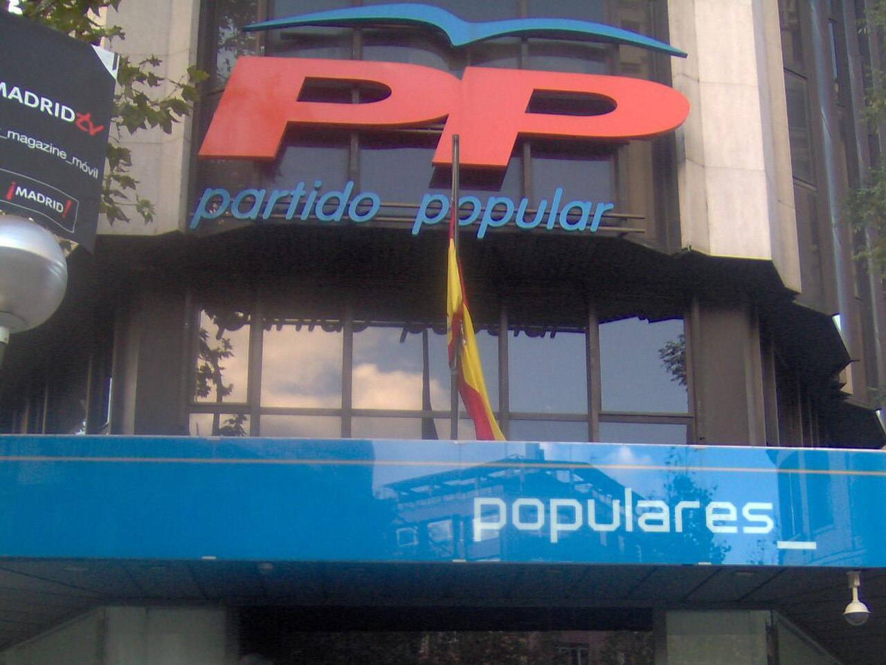 The building facade displays a large red 'PP' logo above the words 'partido popular' in blue. A Spanish flag hangs in front of the windows. Below, a blue sign reads 'populares'.