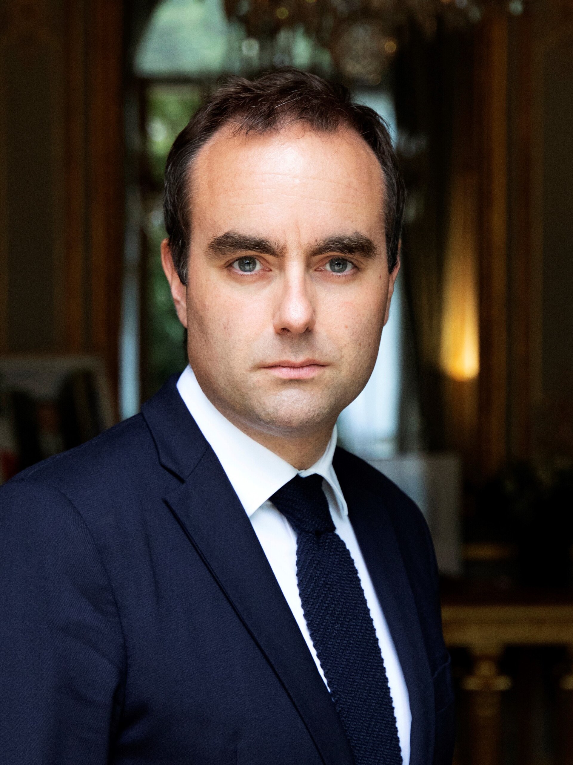 A man in a blue suit and tie looks at the camera.