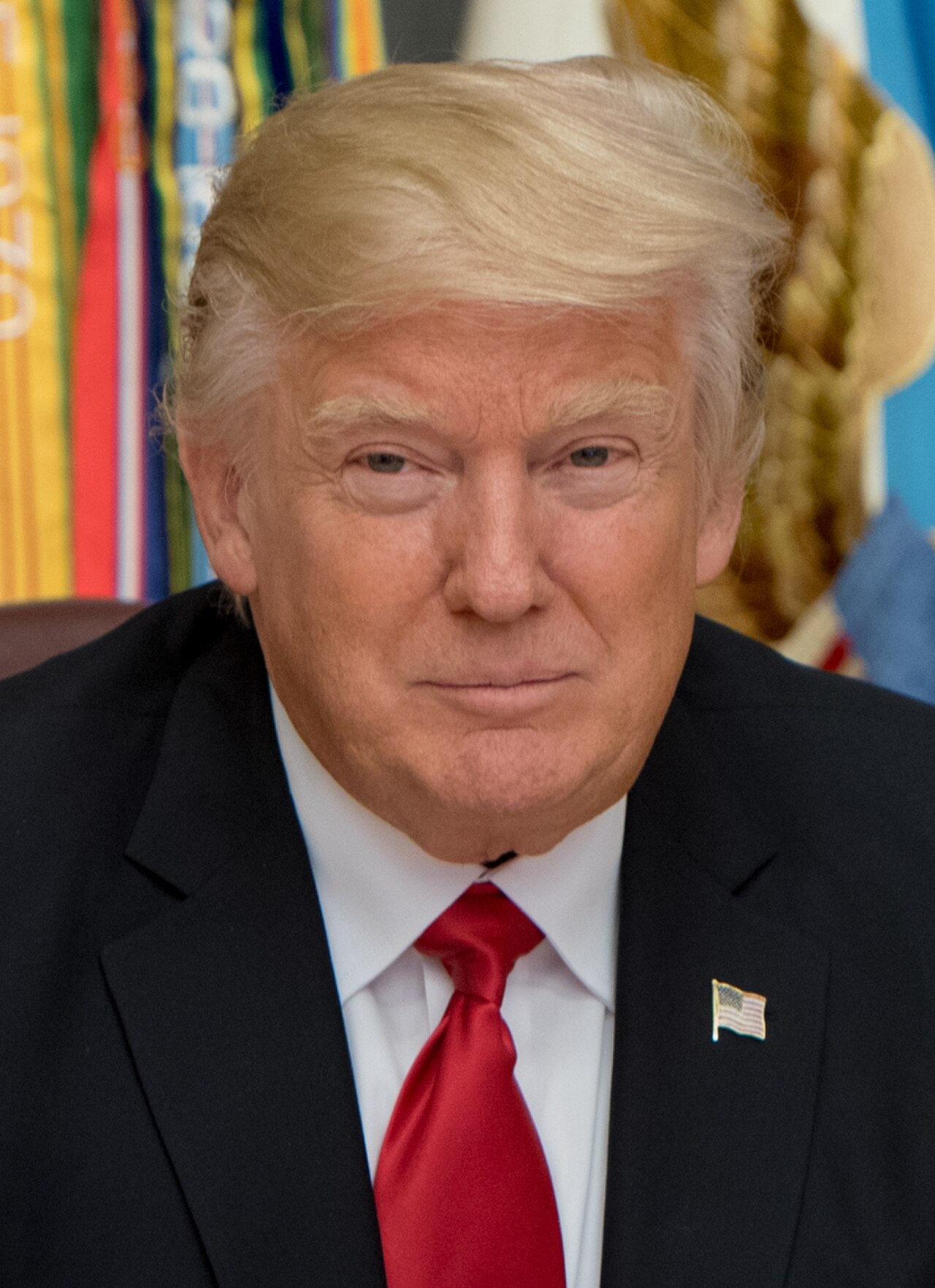 Donald Trump, wearing a black suit, white shirt, red tie, and American flag pin