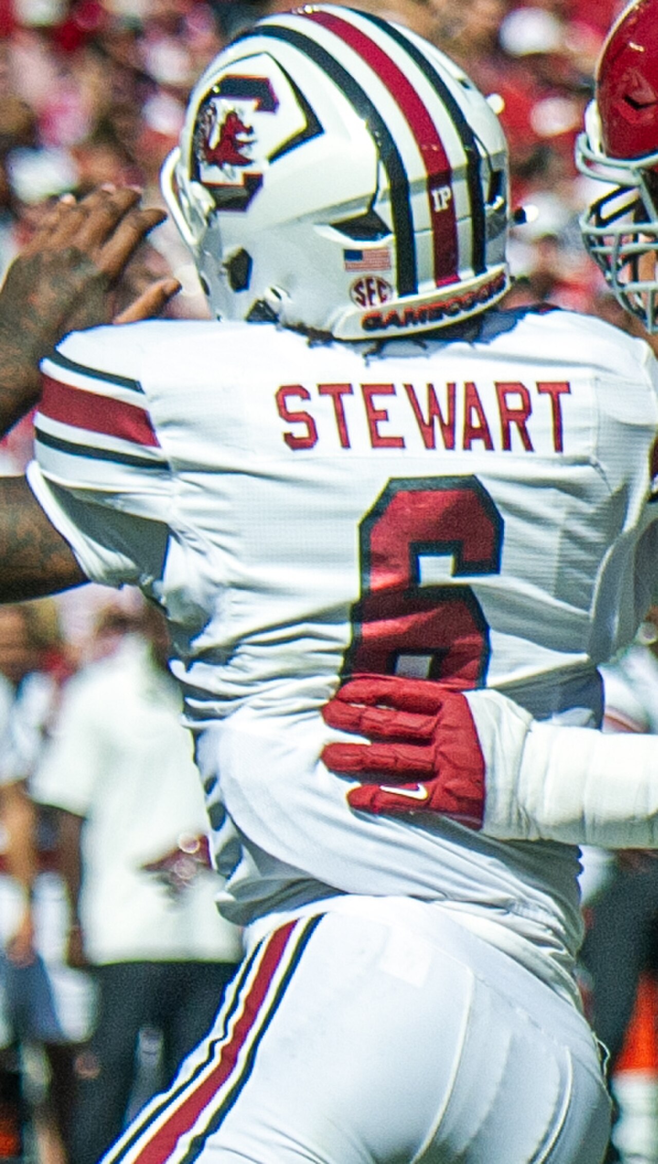 A football player in a white jersey with red and black stripes, wearing a white helmet with red and black stripes, and the name STEWART and number 6 on the back.