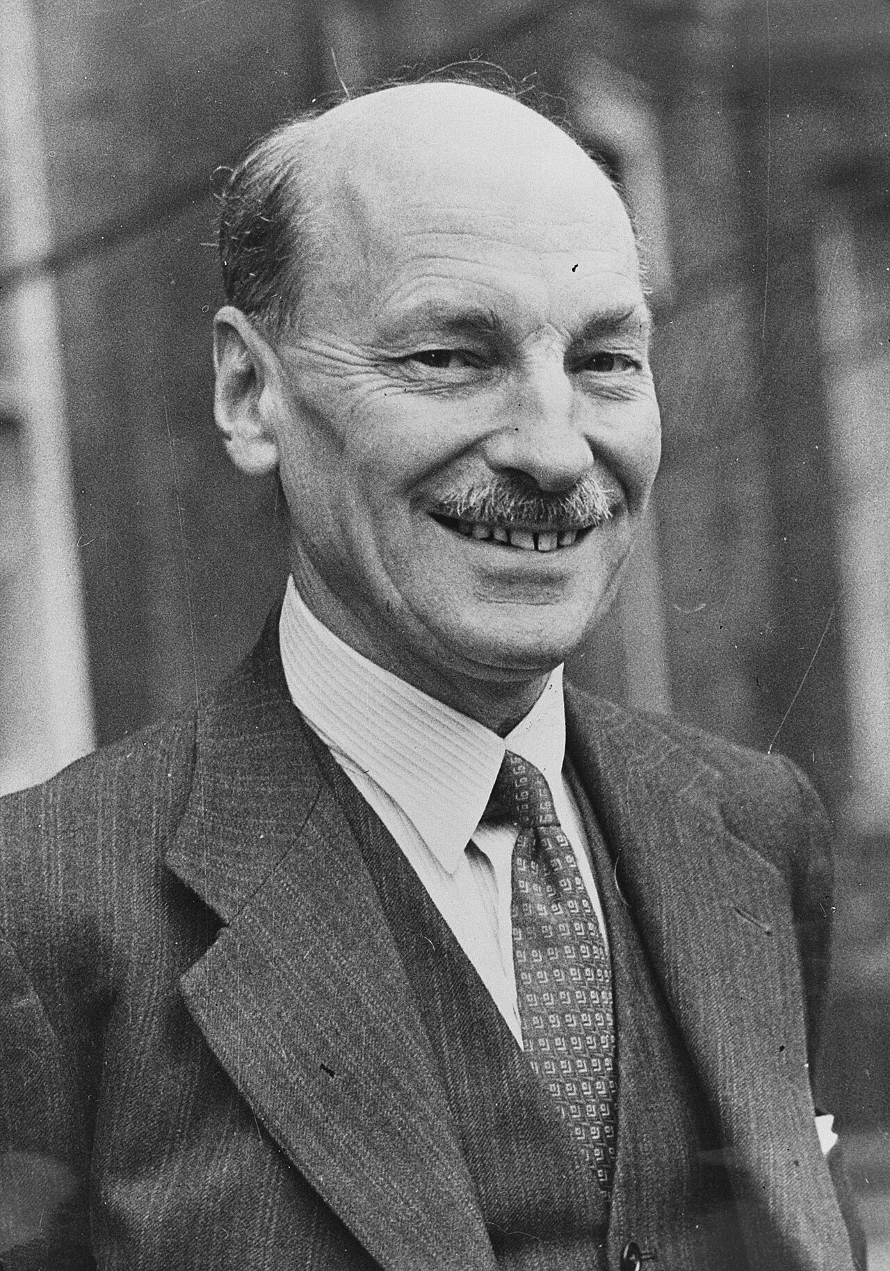 A black and white portrait of a smiling man with a mustache, wearing a suit and tie.