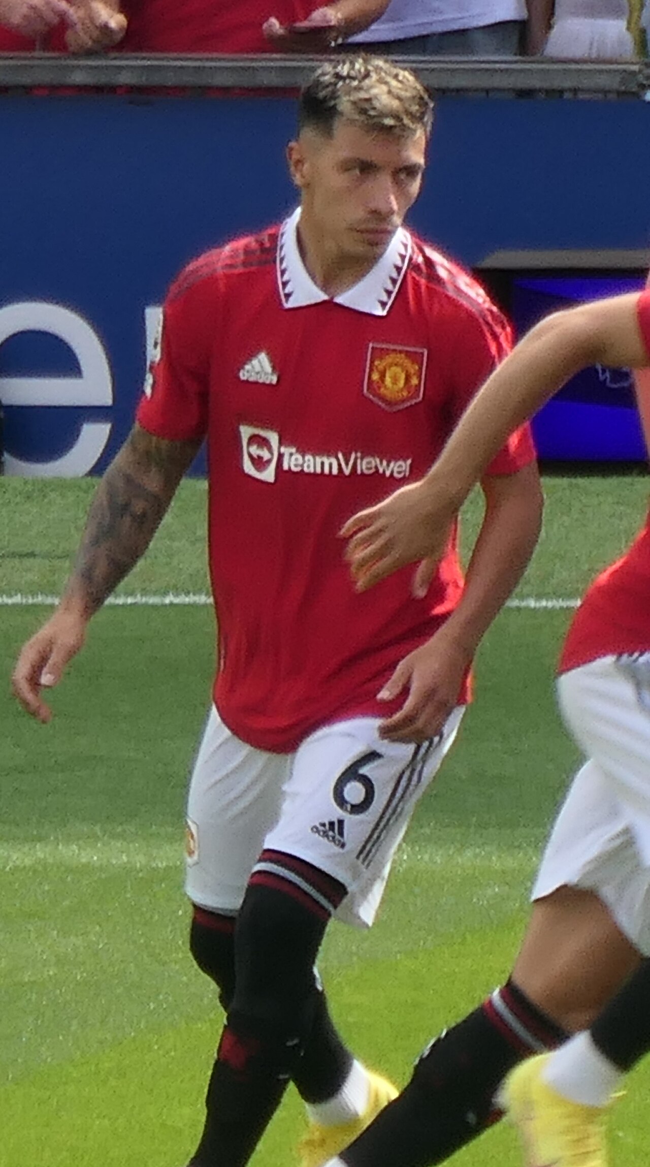 Lisandro Martinez in a Manchester United kit with the number 6 on his shorts, standing on a green field.