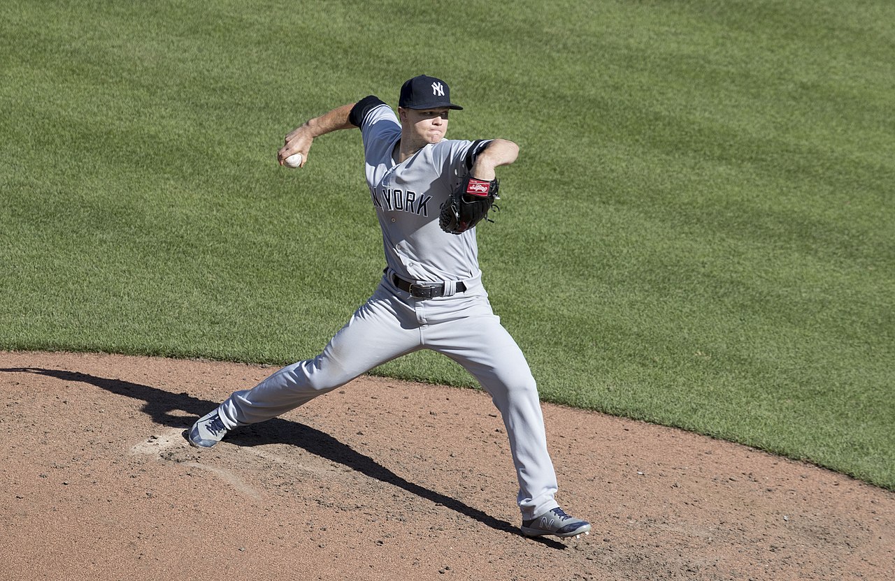 A baseball player in a gray New York uniform pitching on a dirt mound.