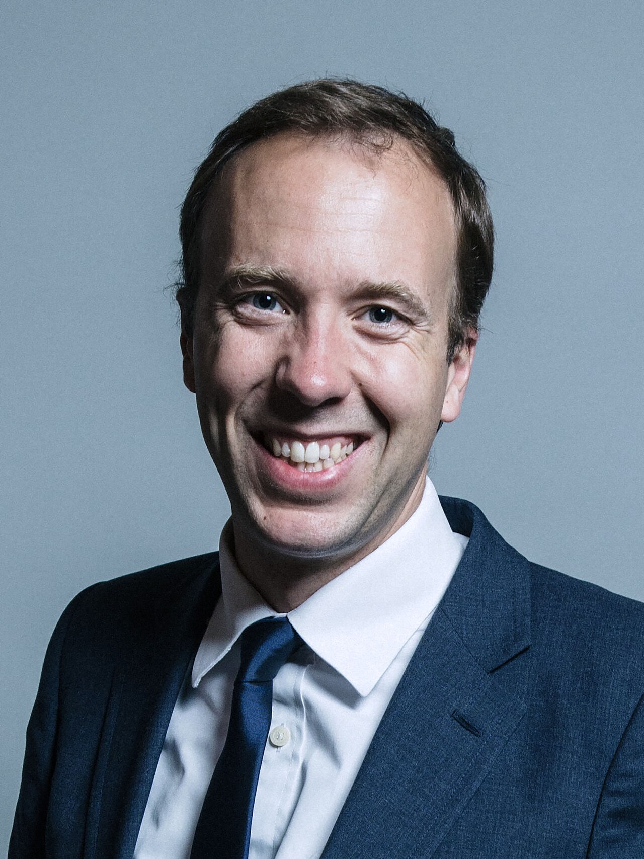A man in a blue suit and tie smiles at the camera.