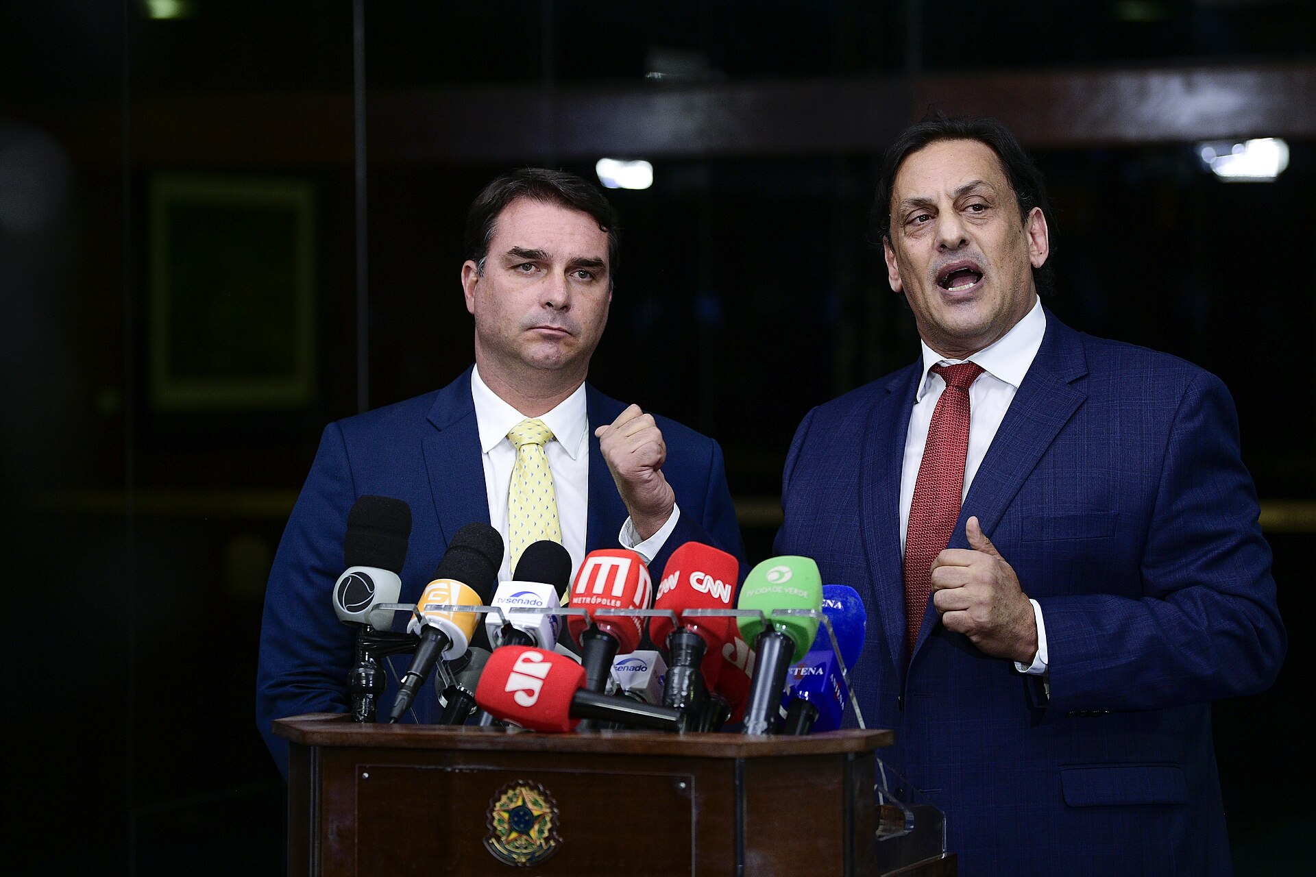 Two men in blue suits standing at a podium with microphones
