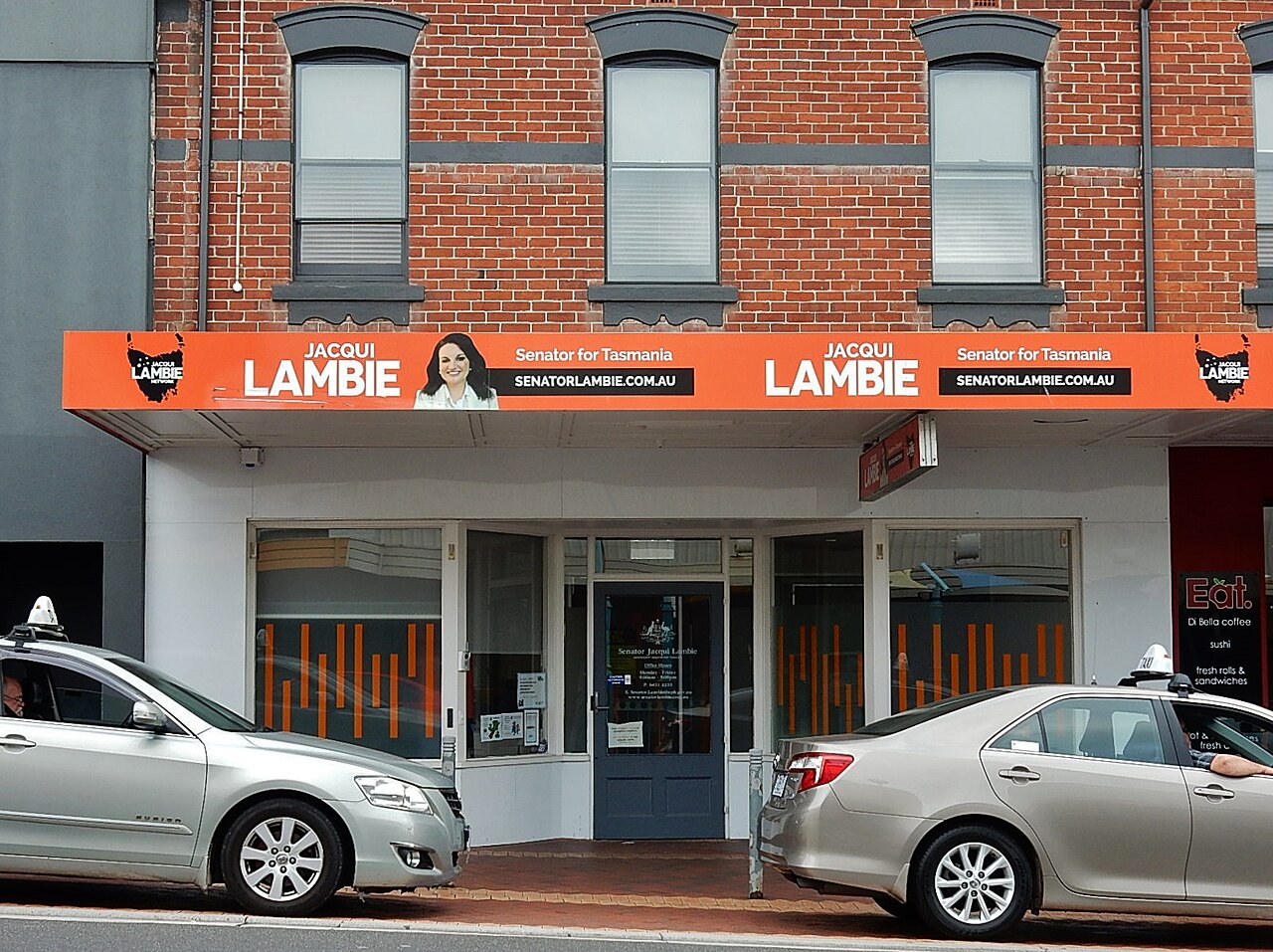 A storefront with an orange banner displaying "JACQUI LAMBIE Senator for Tasmania SENATORLAMBIE.COM.AU" and a photo of Jacqui Lambie.