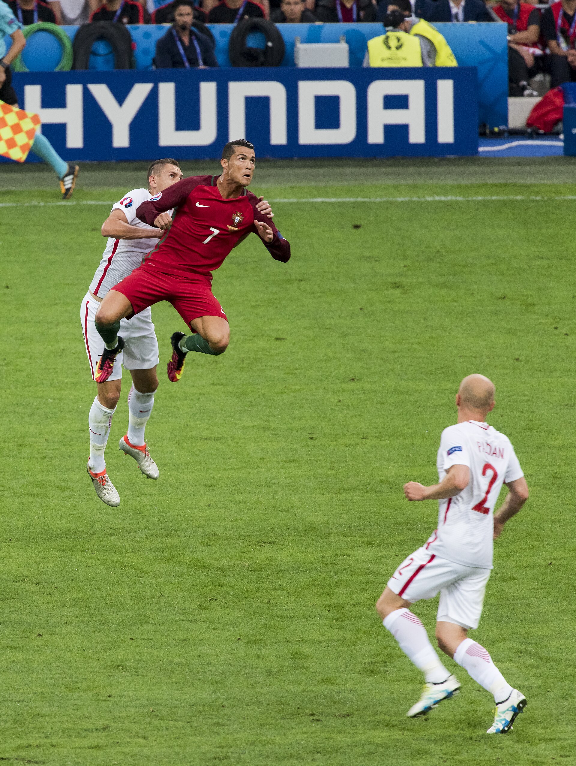 Cristiano Ronaldo in red uniform jumping with a player in white uniform on a soccer field
