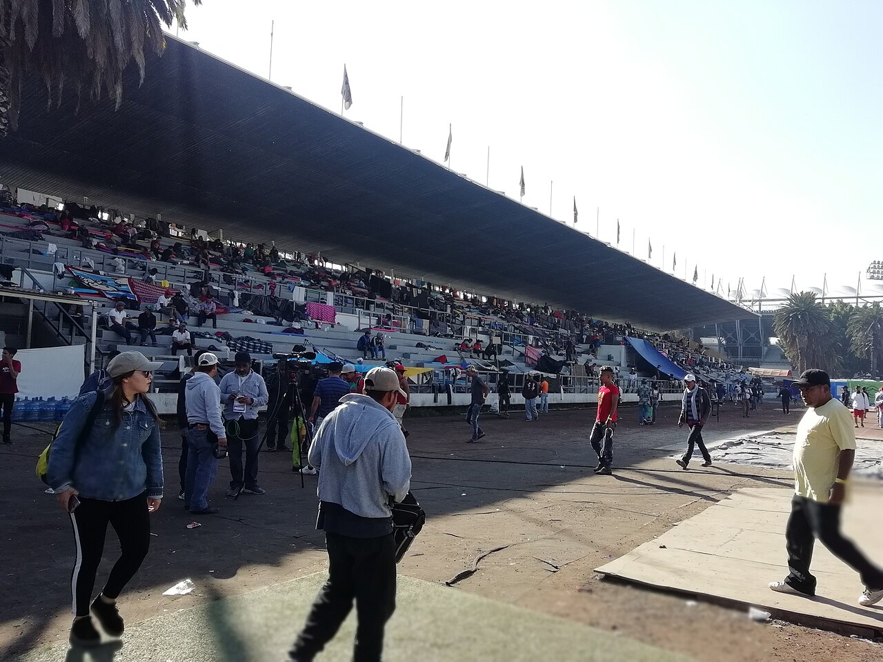 People from a Central American migrant caravan gathered in a stadium in Mexico City in November 2018, with a crowded stand behind them.
