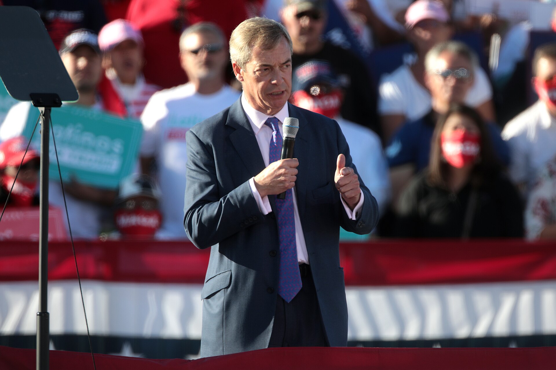 Nigel Farage speaking into a microphone and giving a thumbs up to a crowd.