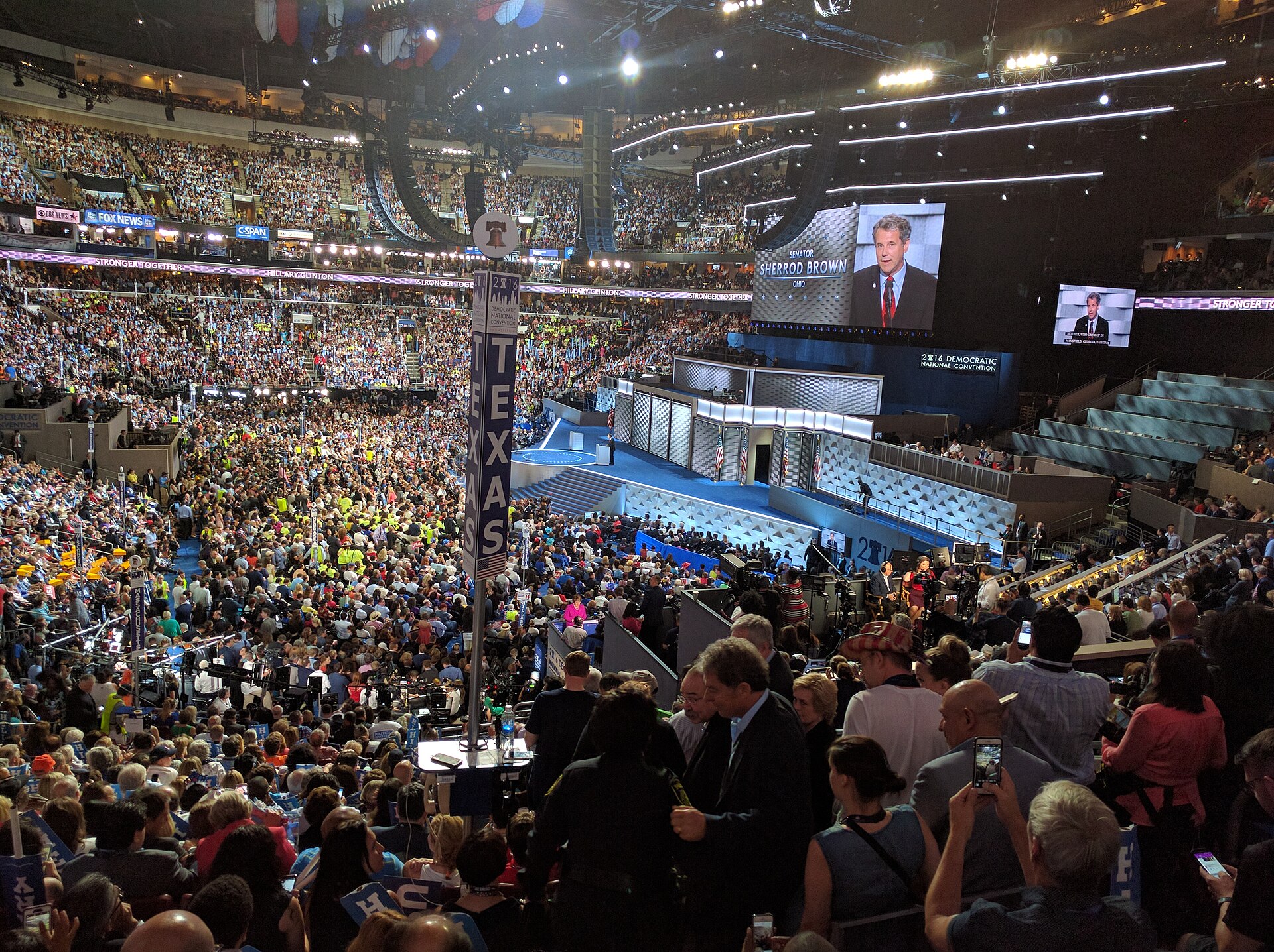A large crowd in an arena with a screen displaying Senator Sherrod Brown