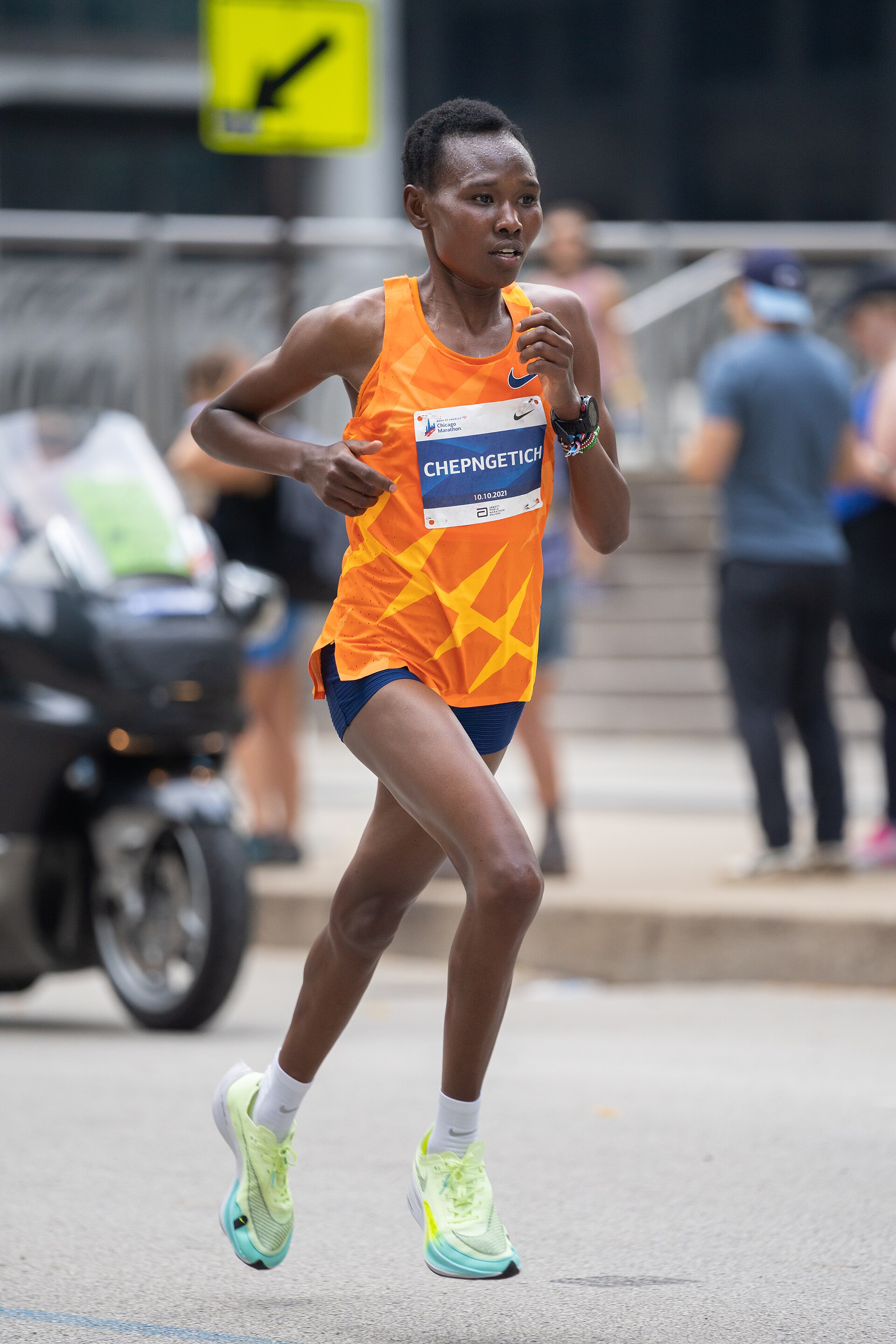 Ruth Chepngetich running in an orange uniform with a race bib