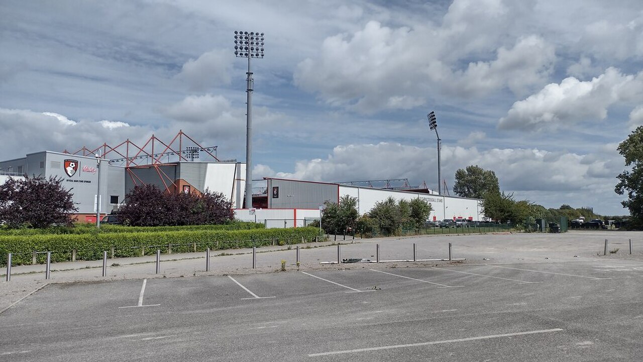 A wide shot of the exterior of a football stadium with a large parking lot in the foreground.