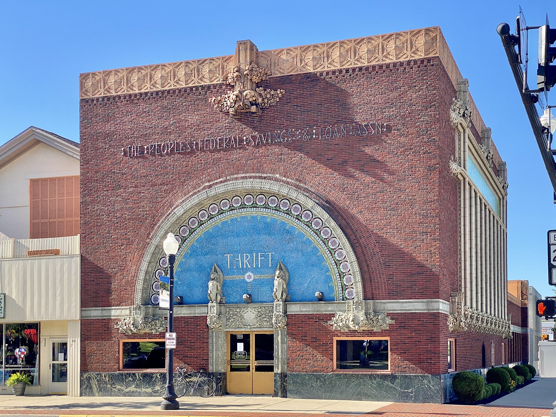 A brick building with ornate architectural details and a large blue mosaic archway above the entrance. The words "THE PEOPLES FEDERAL SAVINGS & LOAN ASSN." are inscribed above the arch, and "THRIFT" is written in the mosaic.