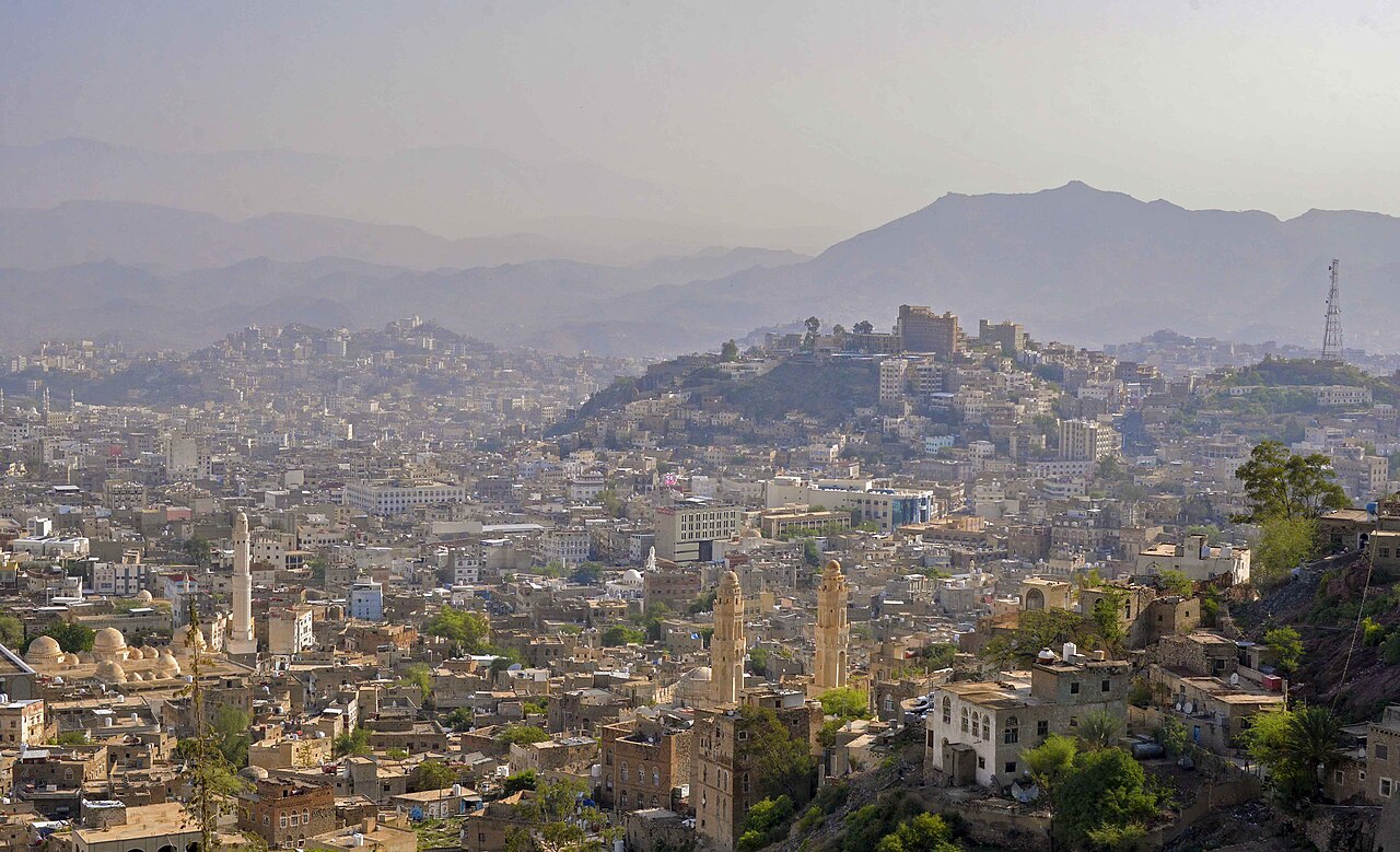 A panoramic view of a densely populated city nestled in a valley, with buildings climbing up hillsides and mountains in the background.