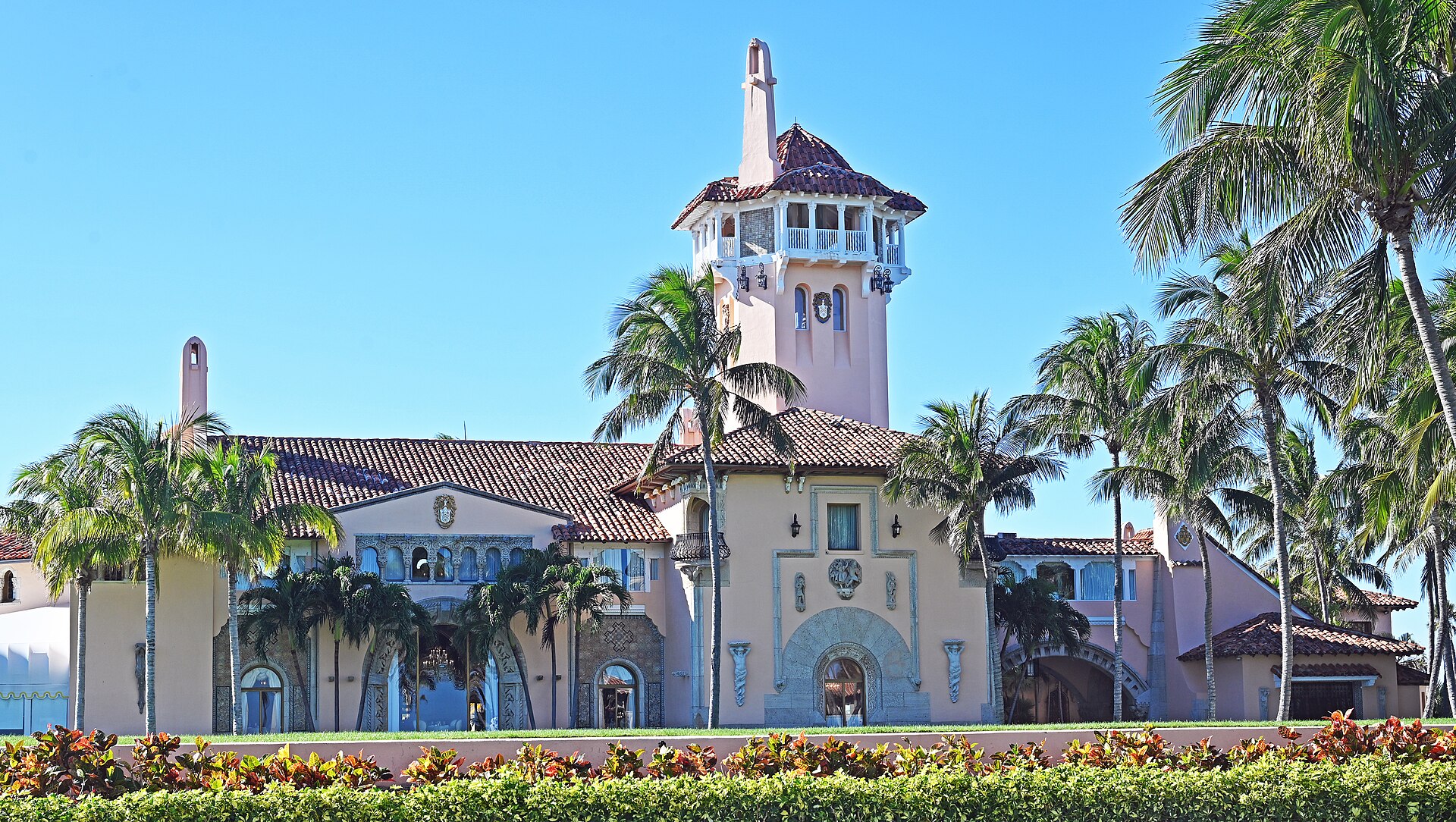 Mar-a-Lago building with tower, palm trees, and ornate facade under a clear blue sky