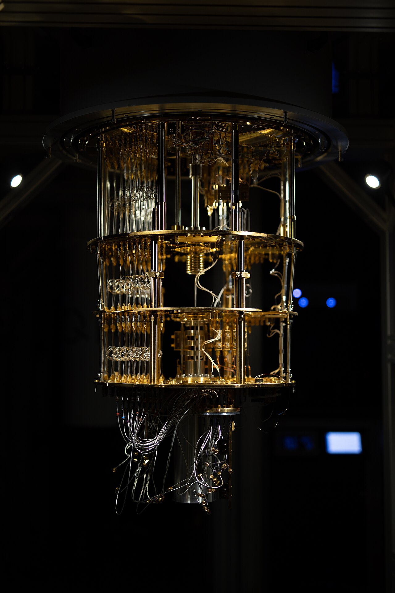 A large, gold-colored quantum computer with wires and tubes attached, in a dark room.