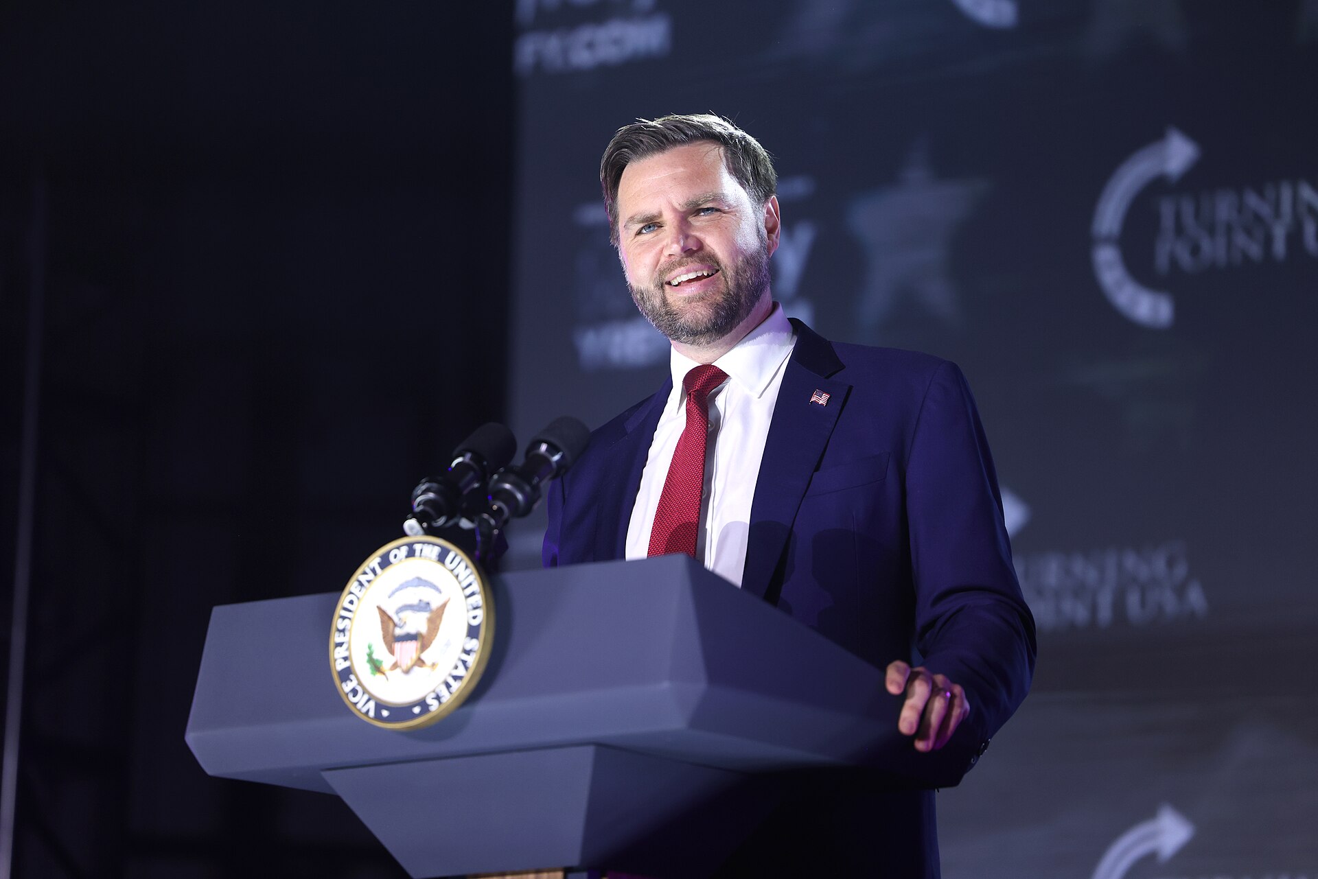 man in blue suit and red tie standing at a podium with the Vice President of the United States seal on it