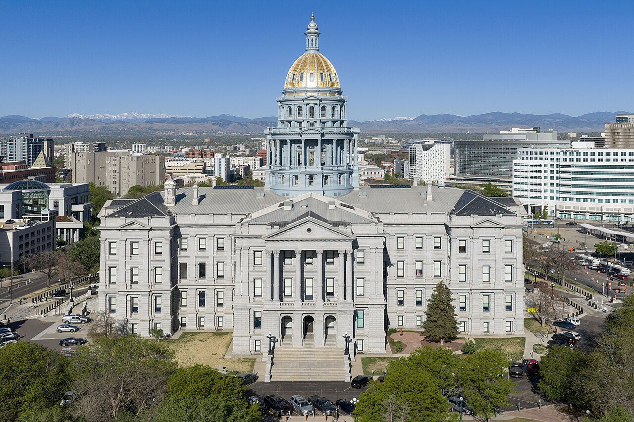 The Colorado State Capitol in Denver, gold dome centered, with the mountains behind it.