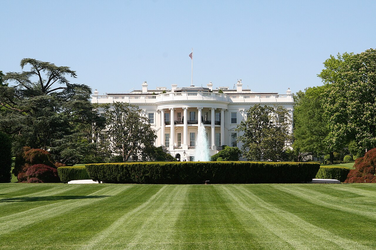 The White House seen from the South Lawn, with the fountain and a trimmed hedge in front.