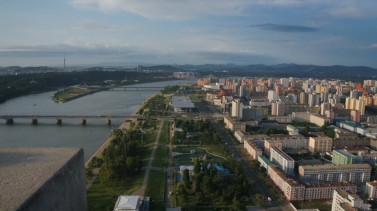 Aerial view of Pyongyang along the Taedong River, with bridges, a television tower, and rows of apartment blocks.