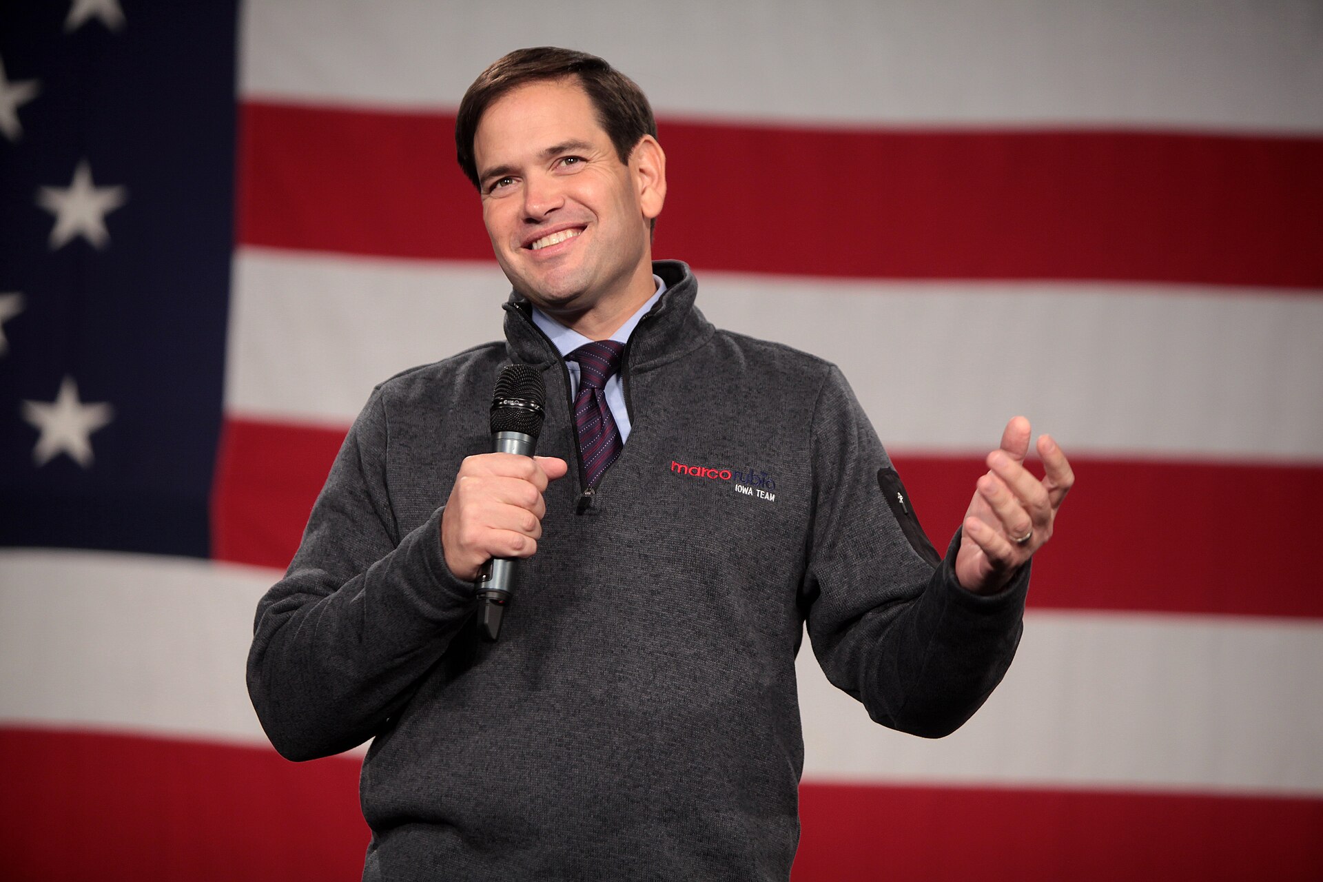 Marco Rubio speaking into a microphone in front of an American flag.