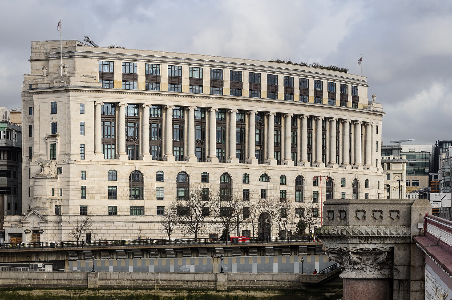 A large, ornate stone building with many windows and columns stands beside a body of water.