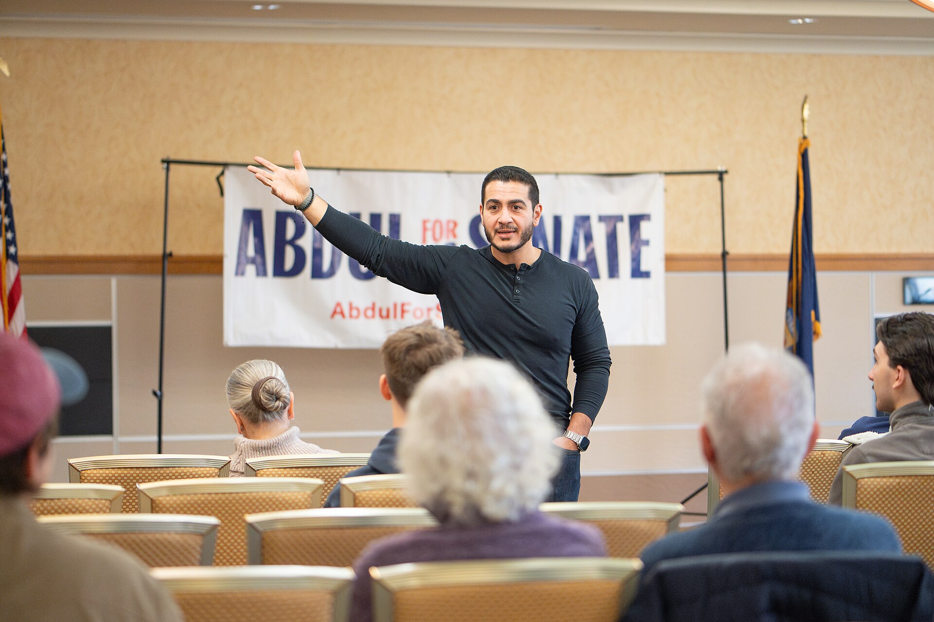A man speaking at a podium with a banner behind him that reads "ABDUL FOR SENATE". He is gesturing with his right hand.