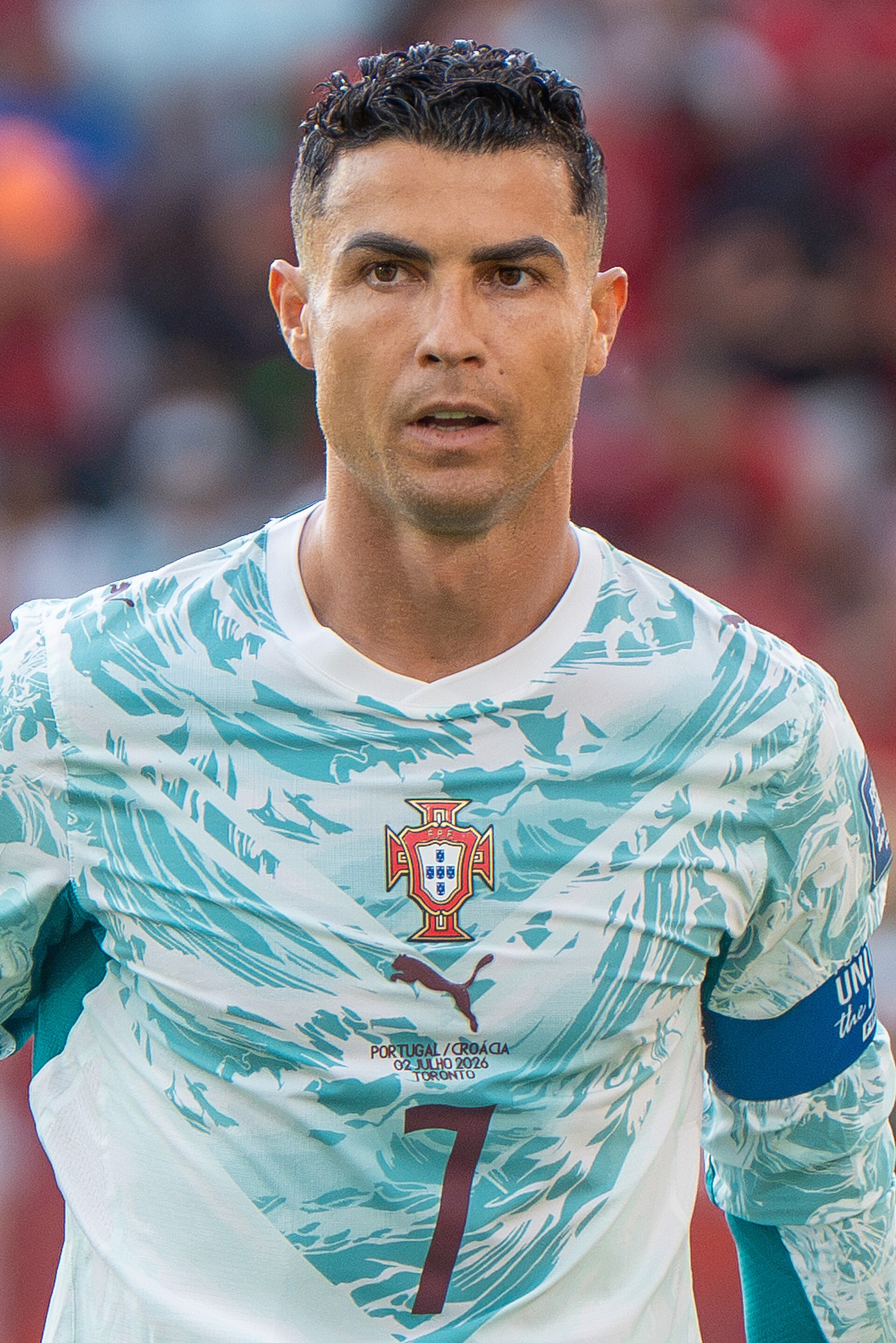 A man with short dark hair wearing a white and light blue soccer jersey with a red, white, and blue shield logo and the number 7 on it.