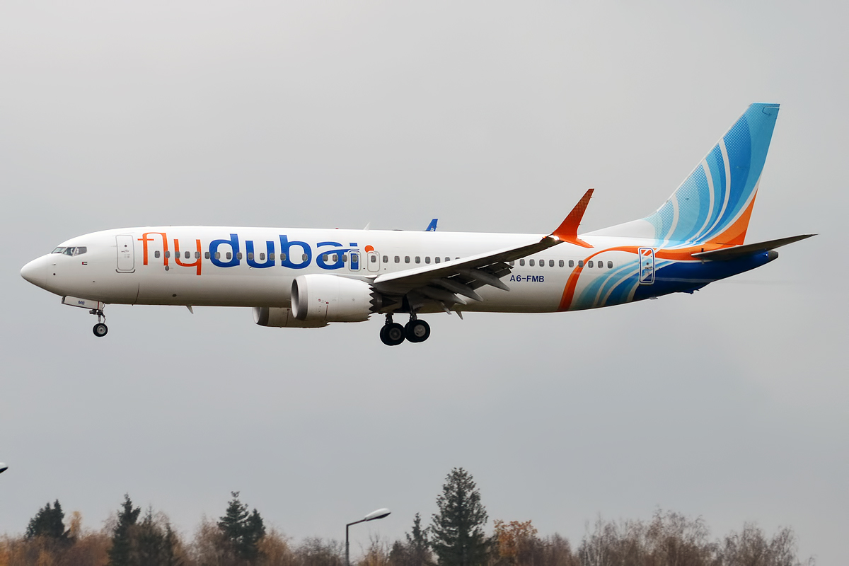 A white flydubai Boeing 737 MAX climbing with the gear down, blue and orange tail, registration A6-FMB.