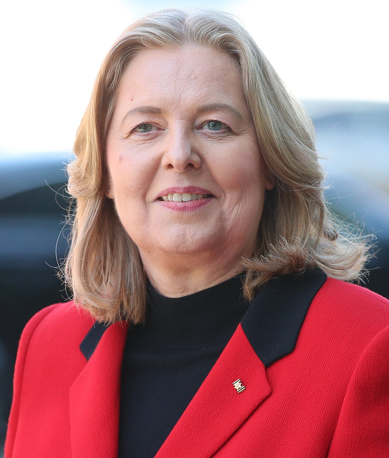 Bärbel Bas, a woman with shoulder-length blond hair in a red jacket over a black top, smiling at the camera.