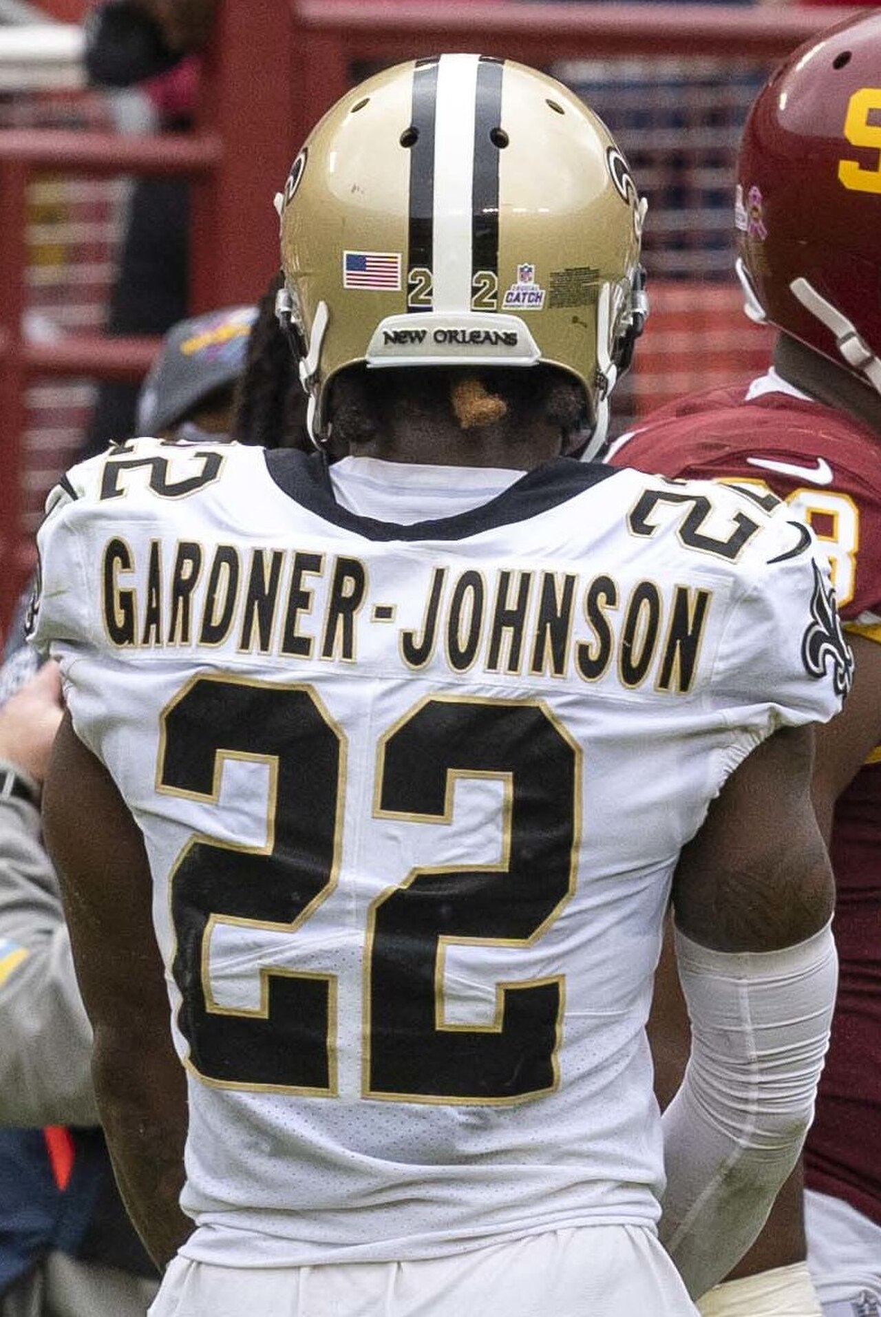 C.J. Gardner-Johnson, wearing a white jersey with black and gold accents, number 22, and a gold helmet with a black stripe, facing away from the camera.