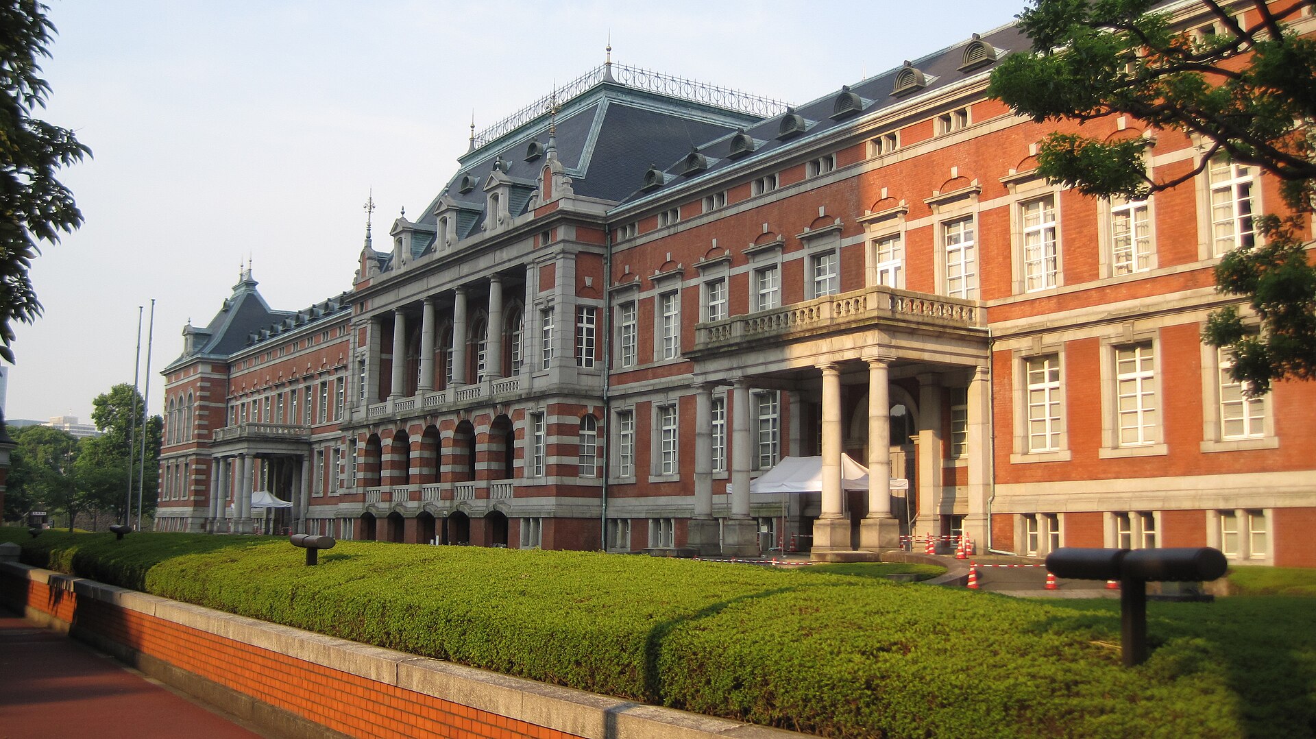 A large, ornate brick building with a dark mansard roof and numerous windows, flanked by columns and a balcony.