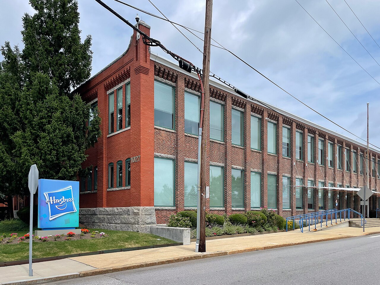 A red brick building with a blue Hasbro sign on the corner of the lawn in front.