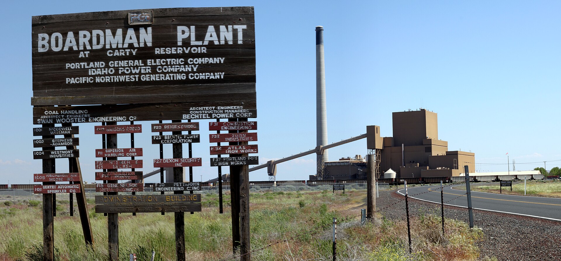 A sign for the Boardman Plant at Carty Reservoir, operated by Portland General Electric Company, Idaho Power Company, and Pacific Northwest Generating Company, stands in front of a large industrial power plant with a tall smokestack.