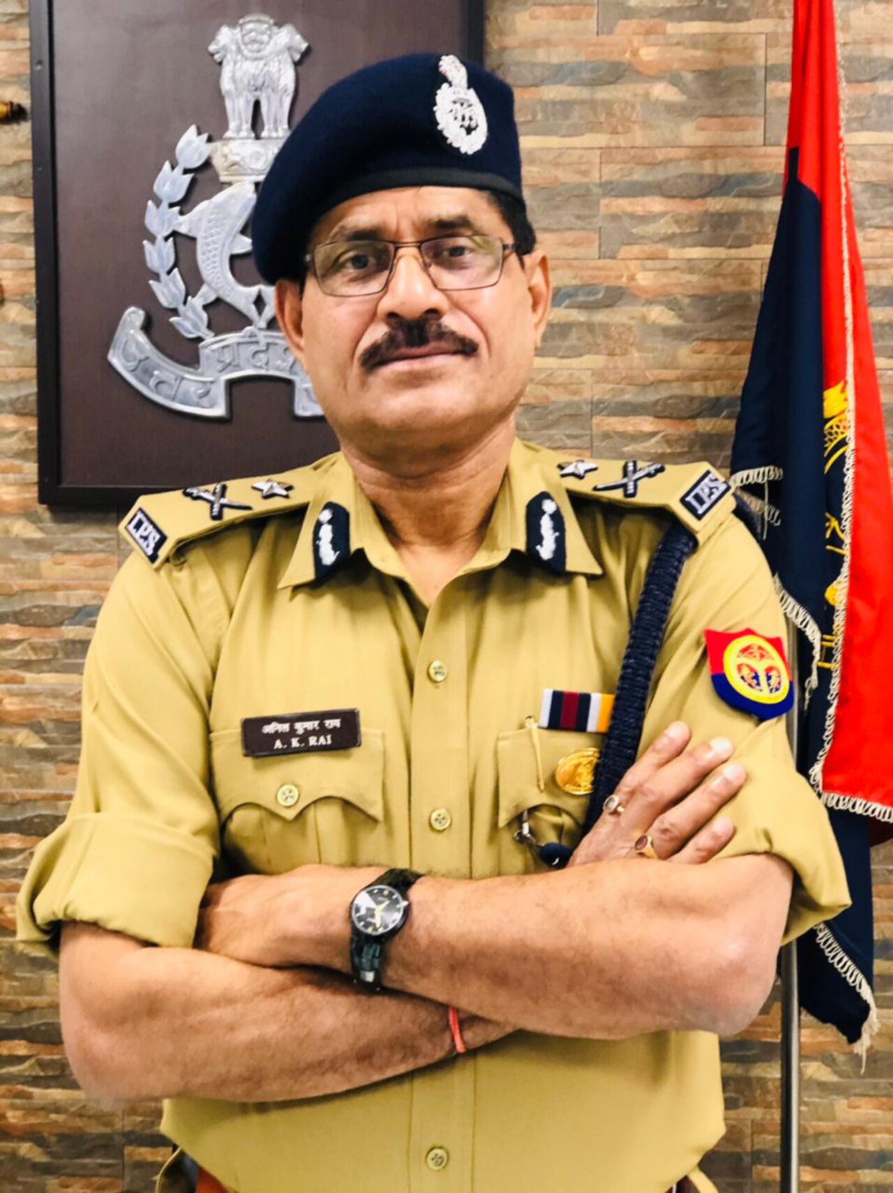 A man in a police uniform with a beret and glasses, arms crossed.