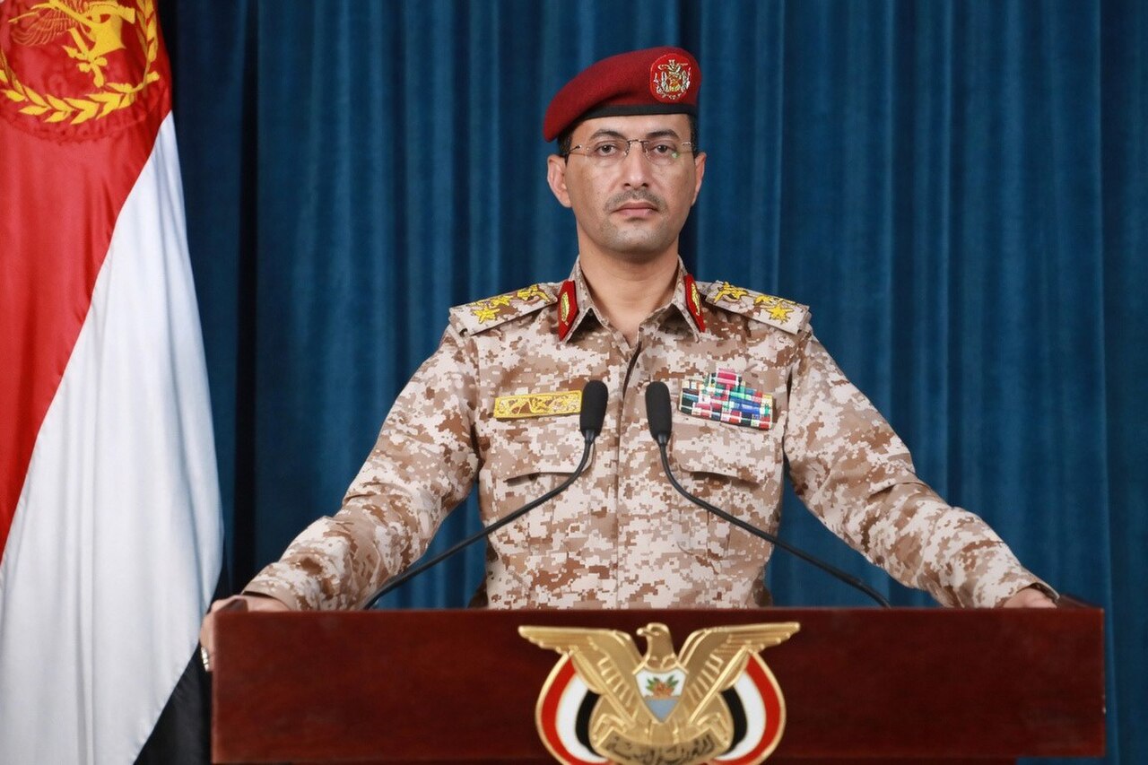 A man in a military uniform stands at a podium with microphones.