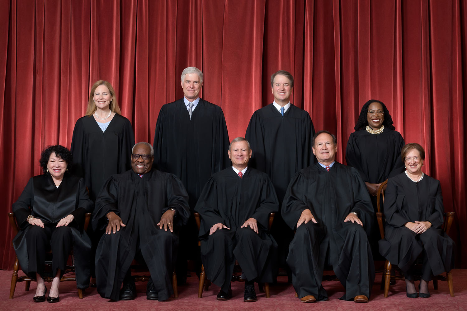 Formal group photograph of the Supreme Court as it was comprised on June 30, 2022 after Justice Ketanji Brown Jackson joined the Court. The Justices are posed in front of red velvet drapes and arranged by seniority, with five seated and four standing. Seated from left are Justices Sonia Sotomayor, C