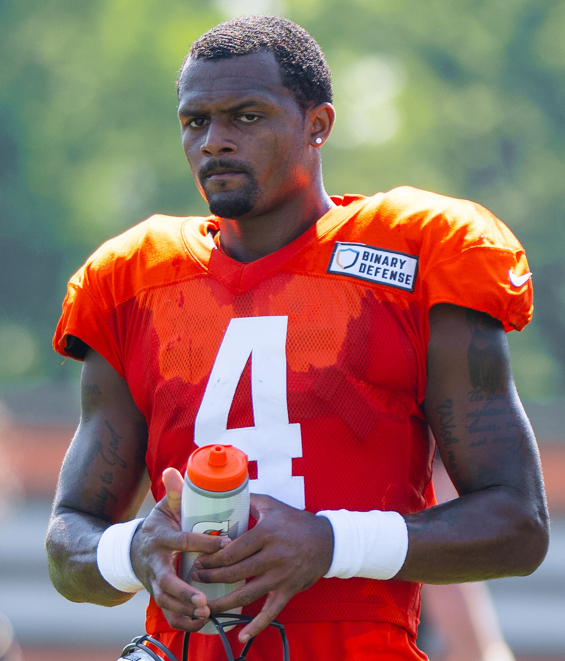 Deshaun Watson, an American football player, wearing an orange Cleveland Browns jersey with number 4, holding a Gatorade bottle.