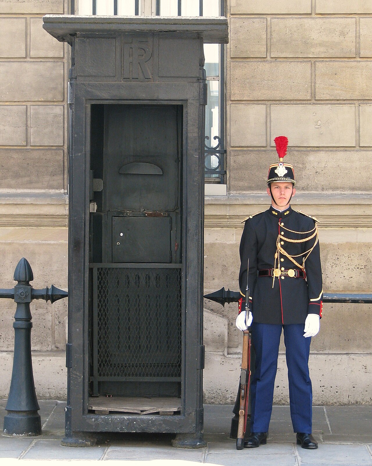 A man in a ceremonial uniform stands guard next to a dark, ornate booth.