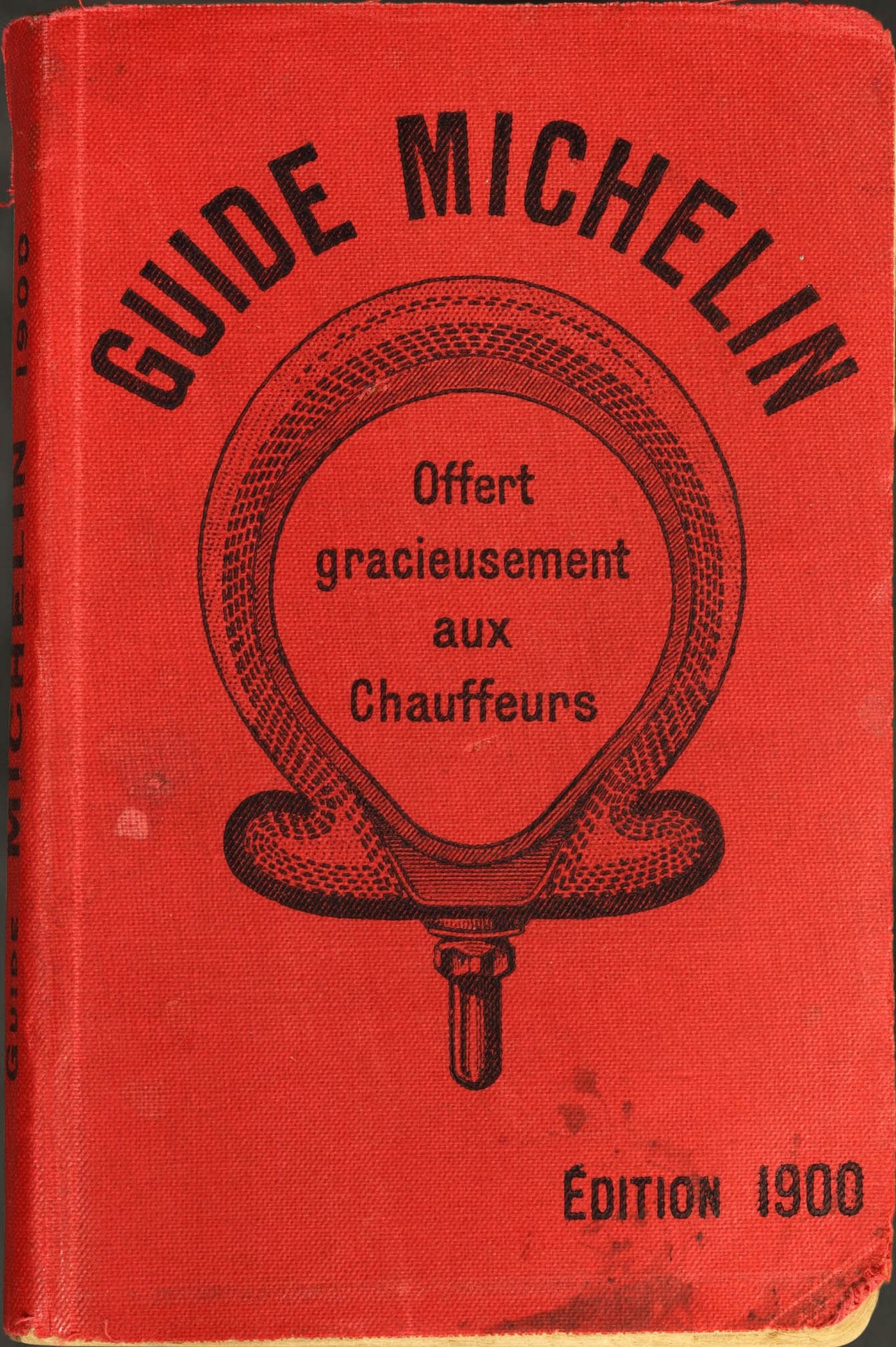 The cover of a red book titled "GUIDE MICHELIN" with "ÉDITION 1900" at the bottom. A circular emblem with text inside is in the center.