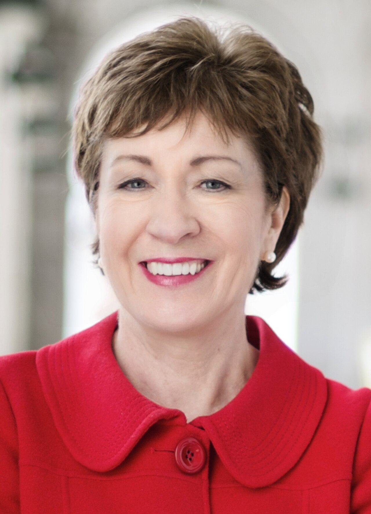 A smiling middle-aged woman with short brown hair wearing a red collared jacket