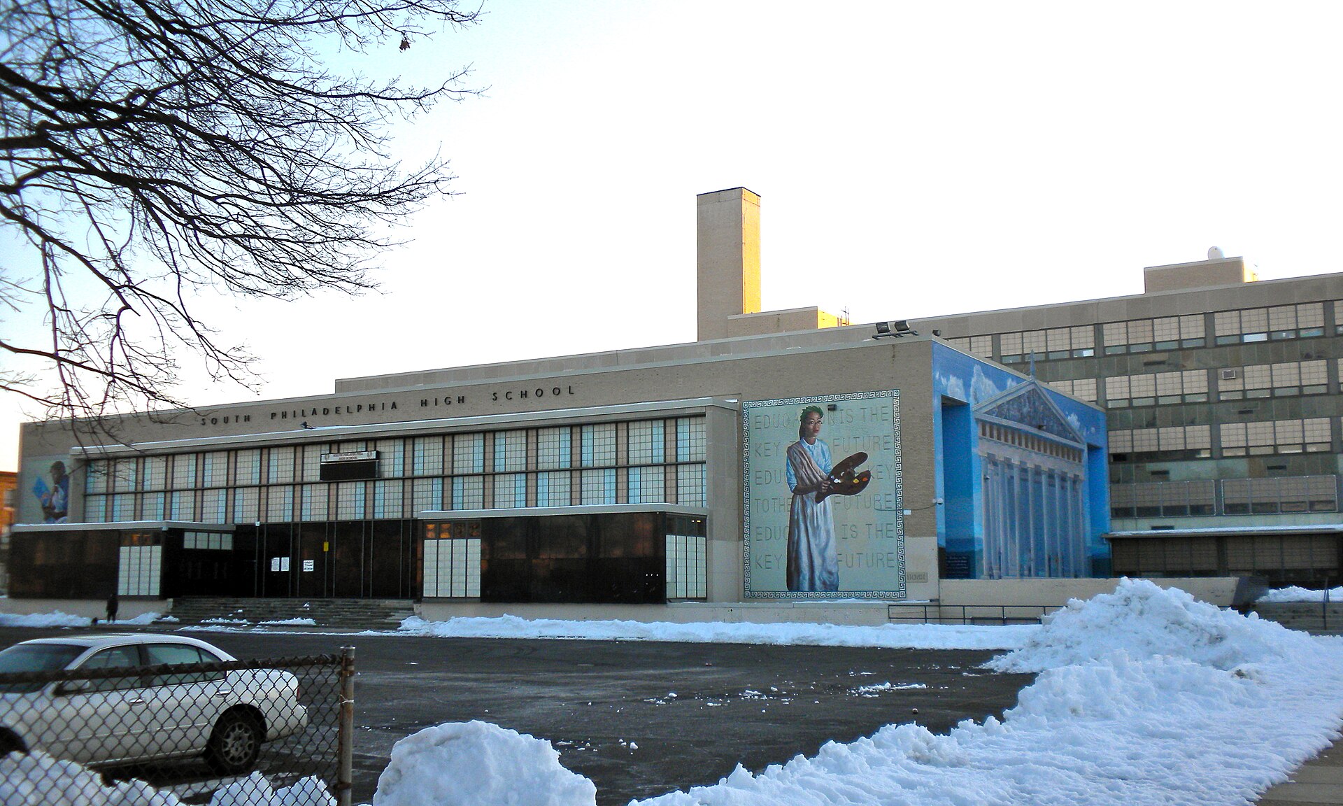 South Philadelphia High School building with a mural of a person holding an artist's palette and a mural of a Greek temple.