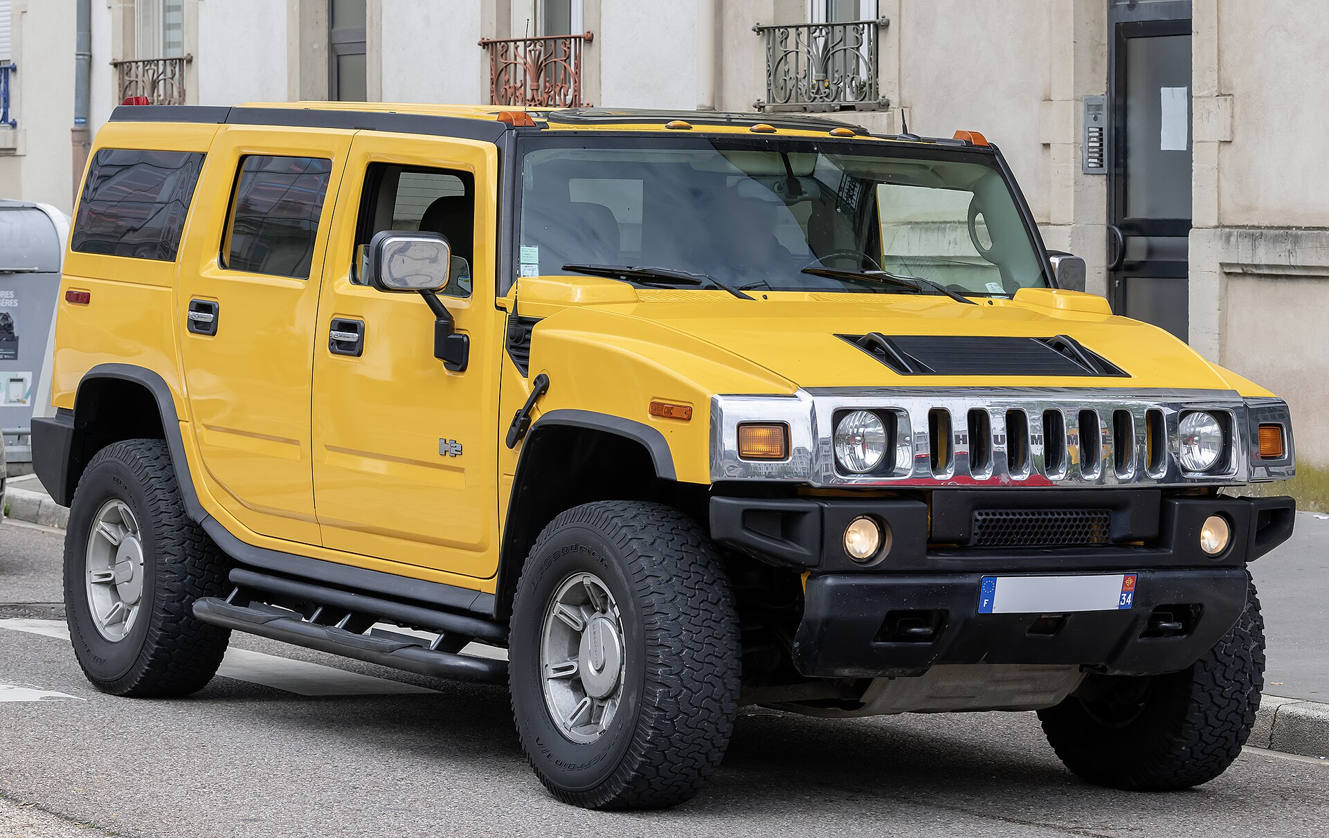 A yellow Hummer H2 SUV is parked on a street, with its front grille and headlights clearly visible.