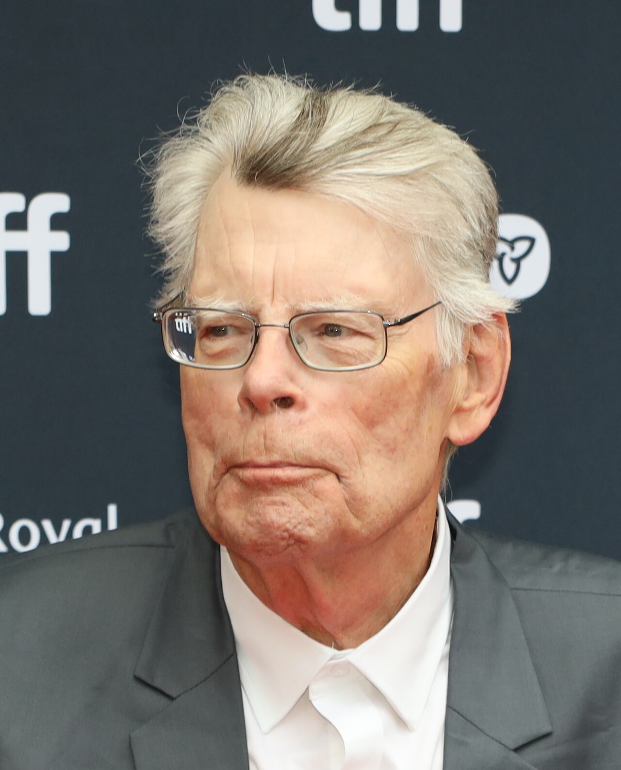 A man with short gray hair, wearing glasses, a white shirt, and a gray suit jacket.