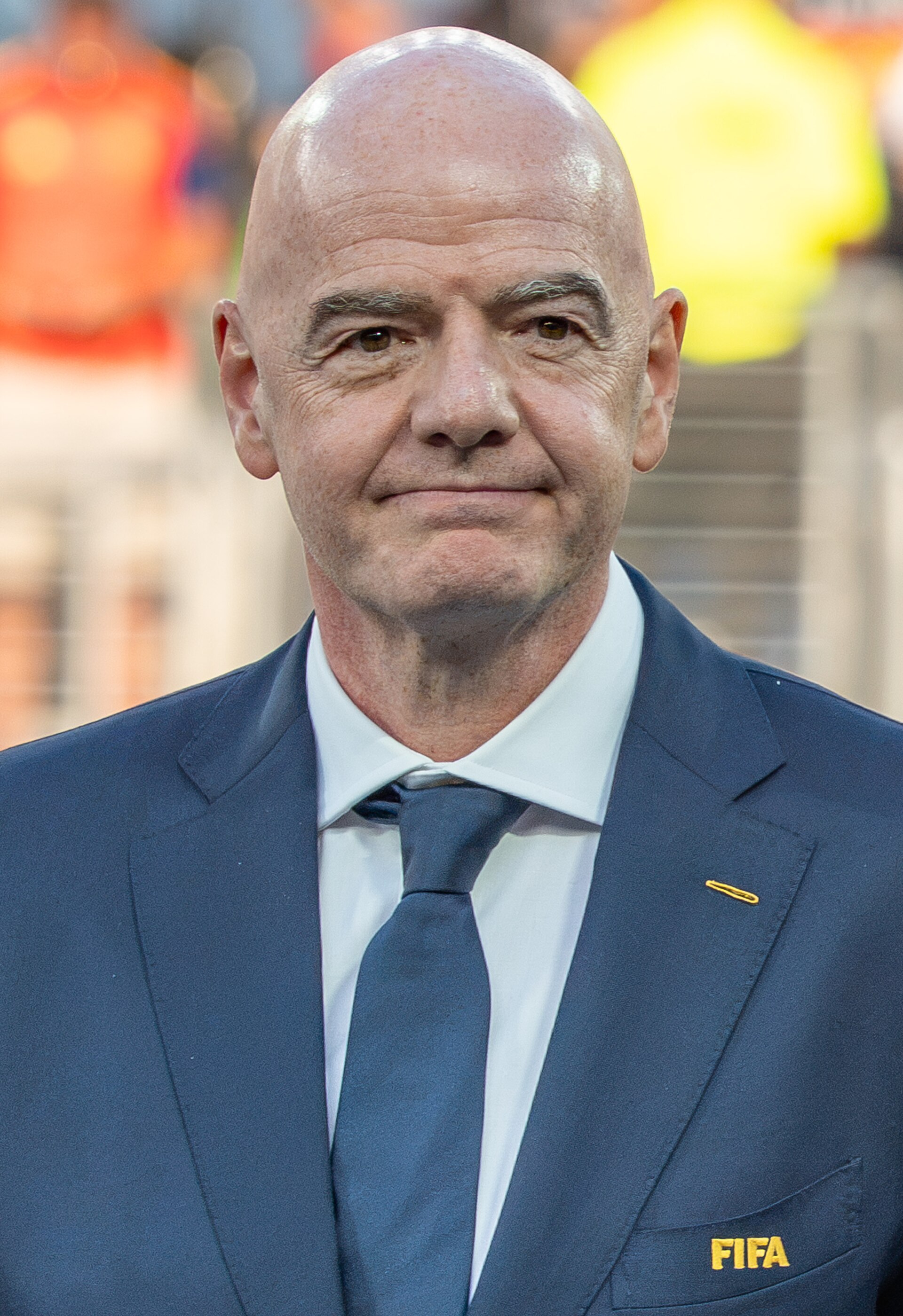 A bald man in a blue suit with a FIFA pin on his lapel